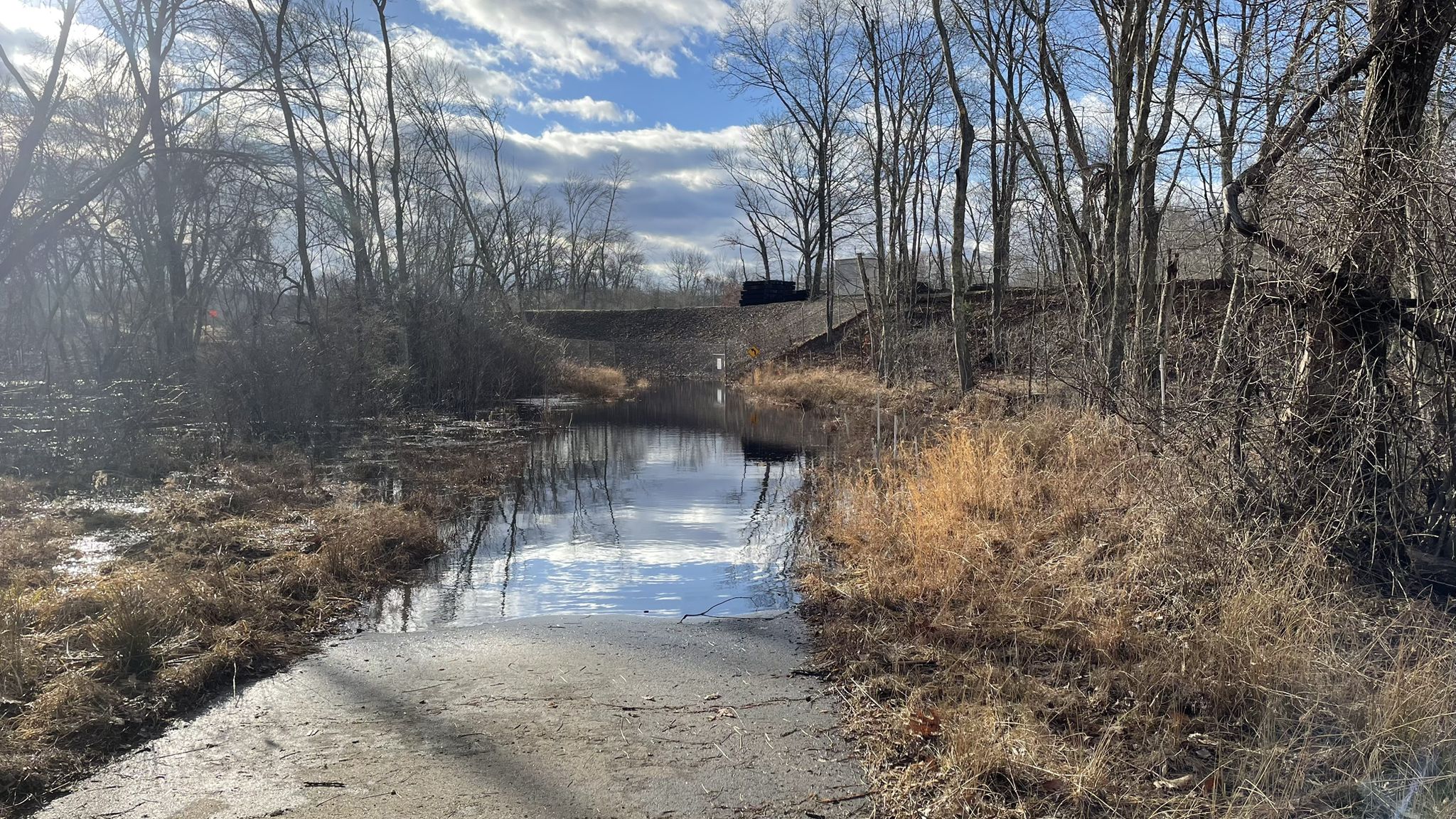Flooded dirt path leading into a calm body of water under a cloudy sky. - Andover Memorial Bridge – Andover loop from Willimantic