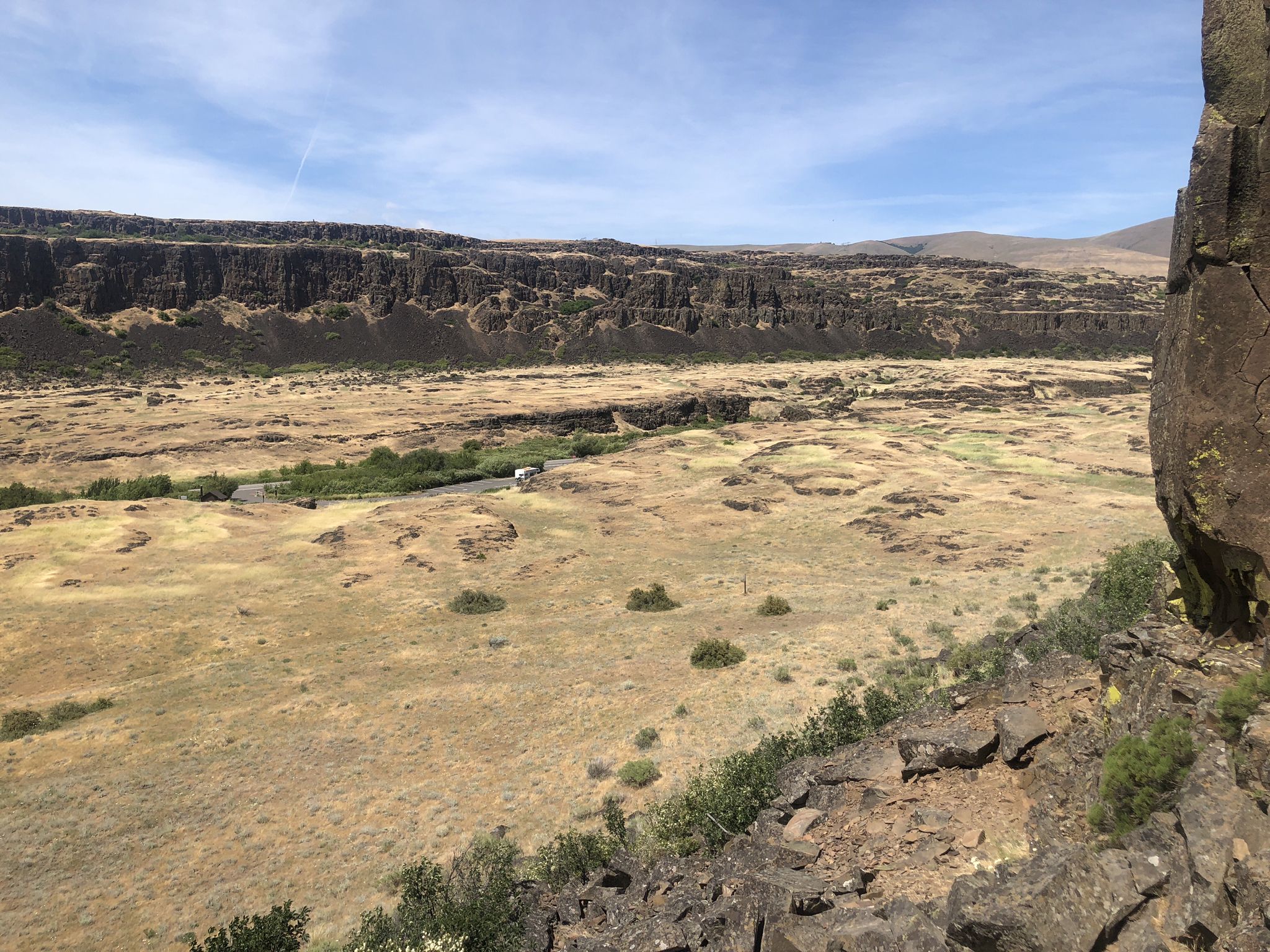 Wide, dry valley with a winding river and distant cliffs under bright sky. - Horsethief Butte Trail