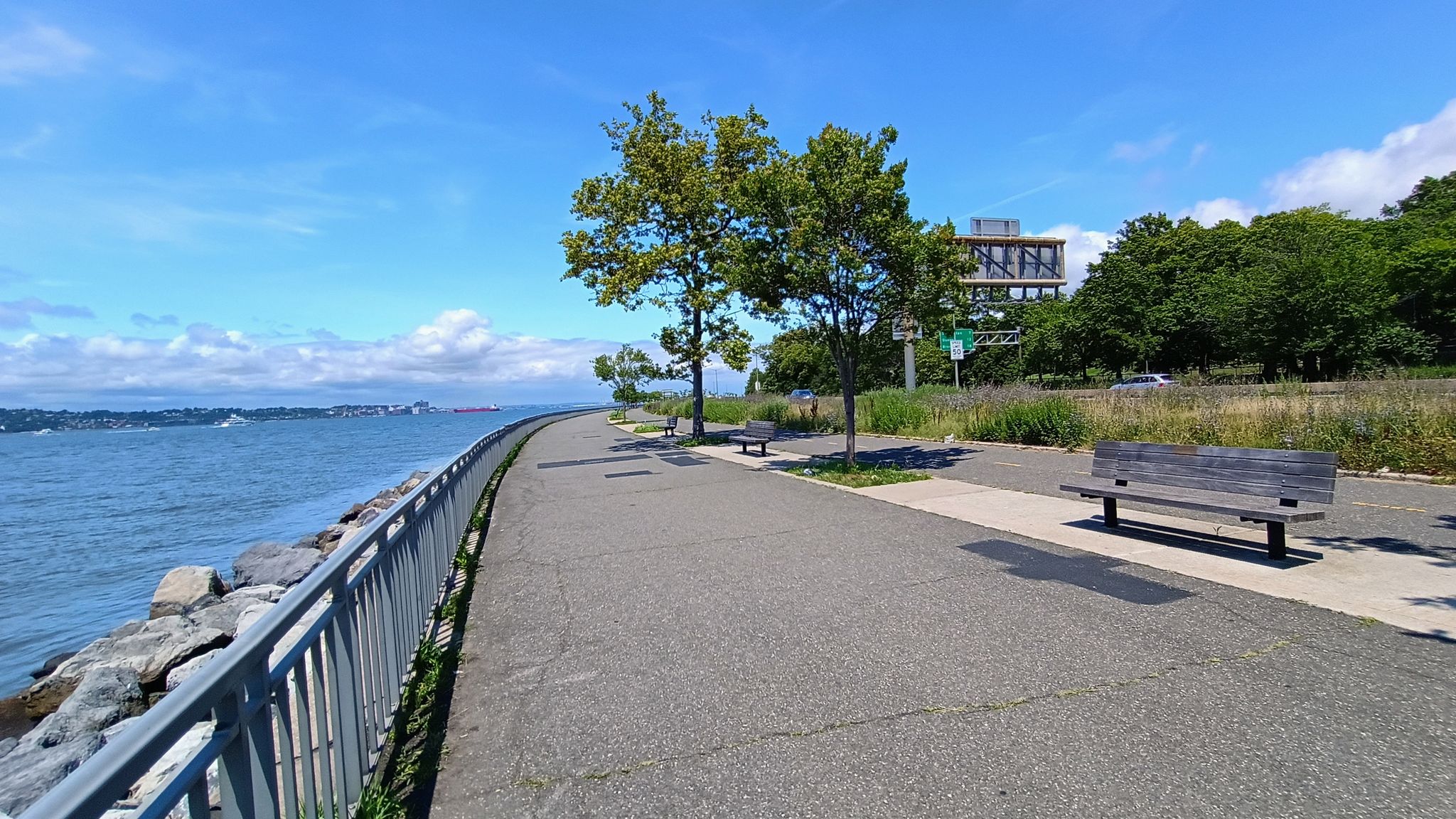 Sunny paved promenade along wide water with trees and empty benches. - Belt Parkway Bike Path loop from Bay Ridge Avenue