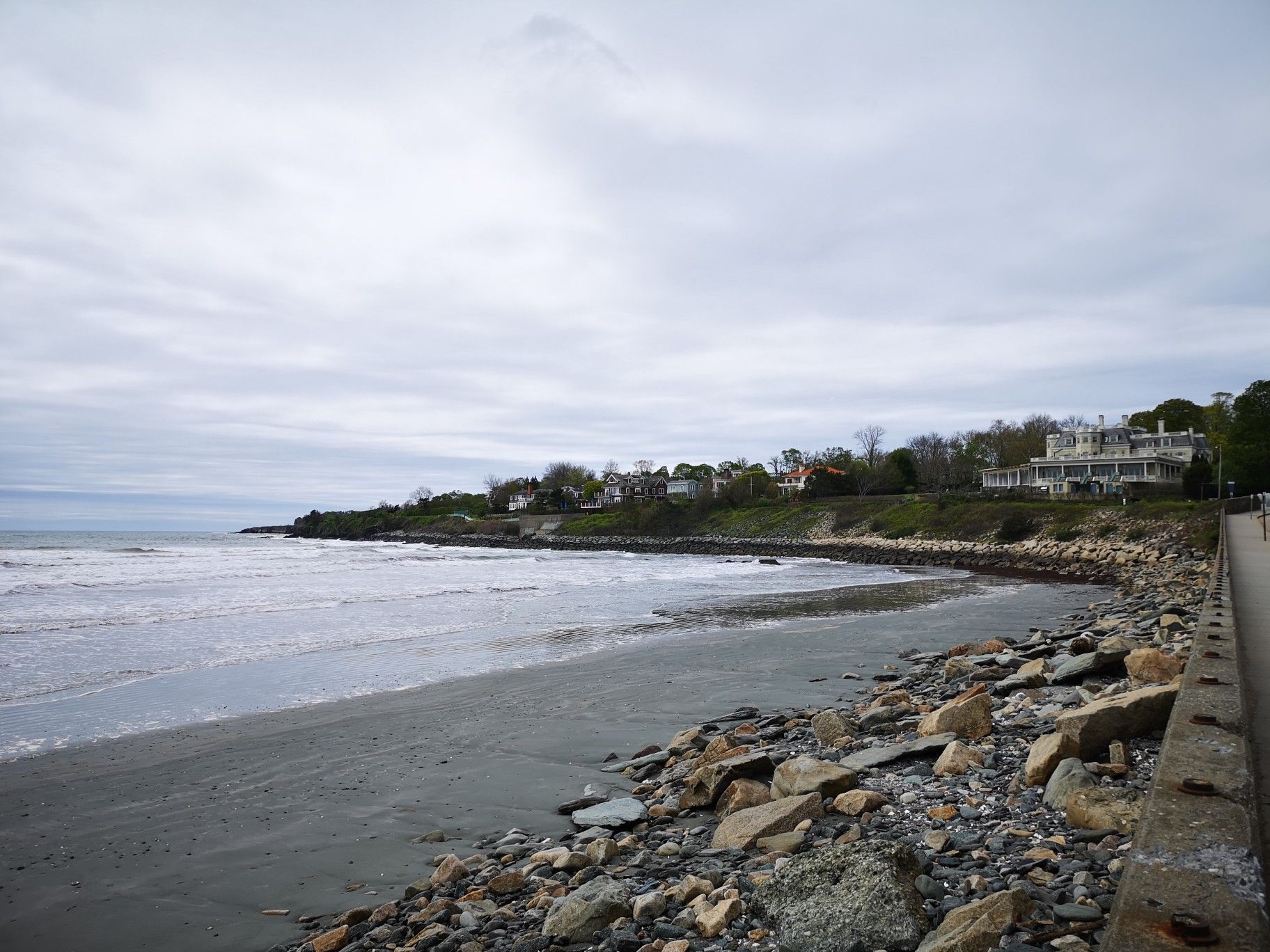 Overcast day at a sandy beach with waves and houses on a distant hill. - Sachuest to Brenton Point via Ocean Drive Scenic Road