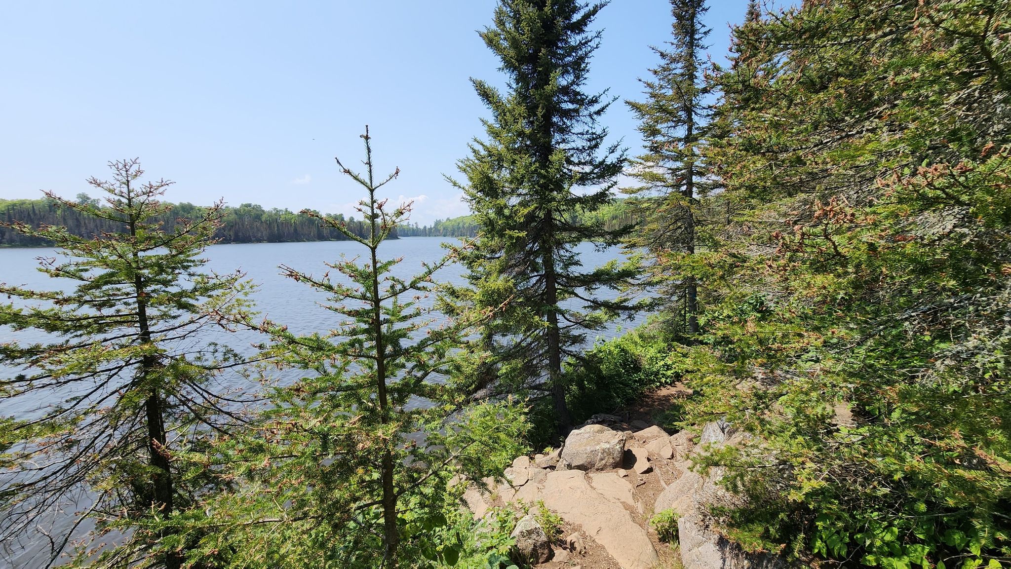 Pine trees frame a large lake on a bright, sunny day. - Superior Hiking Trail to Lake Agnes