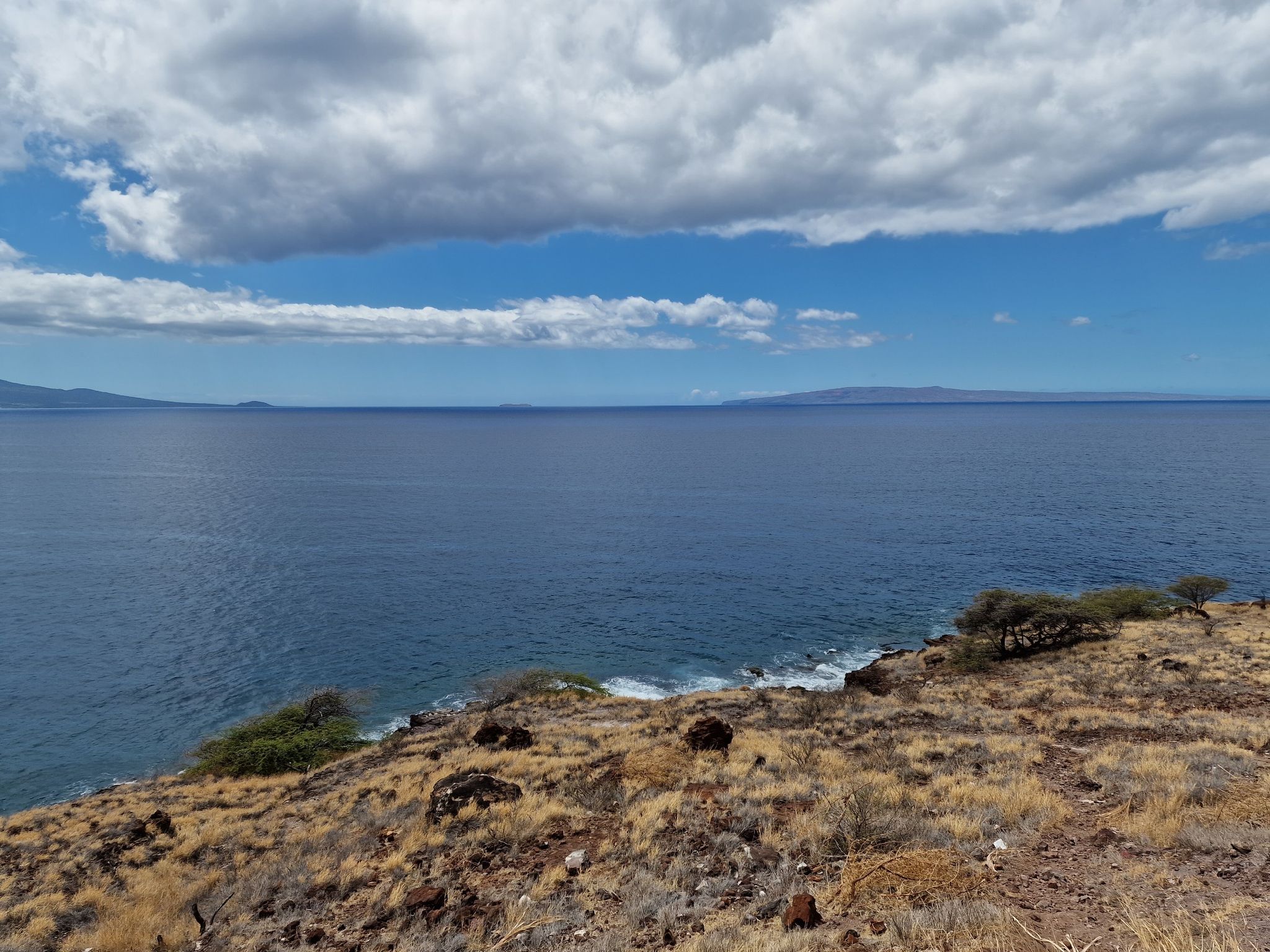 Vast blue ocean under a partly cloudy sky, with dry, rocky foreground. - Old Honoapiilani Highway Trail
