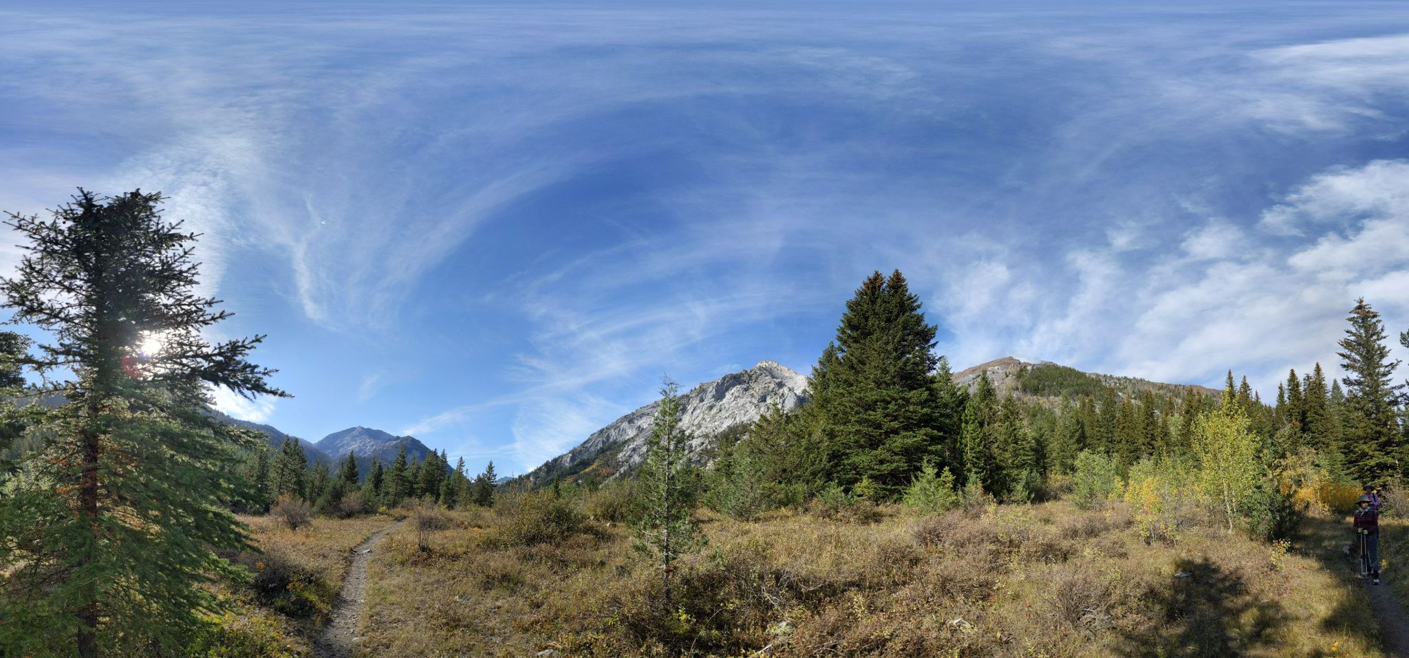 Panoramic view of a mountain valley with forests, a path, and a person. - Sacajawea Peak Trail