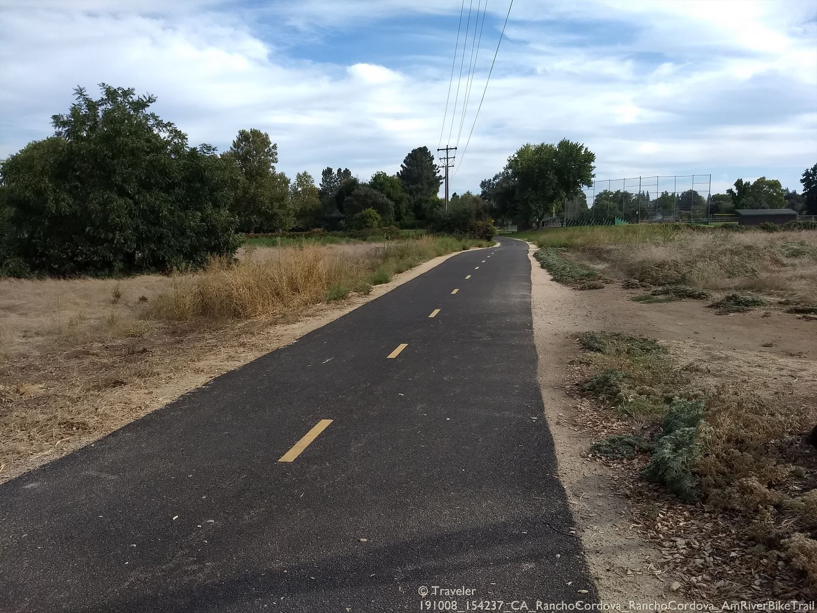 Paved path winding through dry grass and trees under a cloudy sky. - American River – American River Bike Trail loop from Rancho Cordova