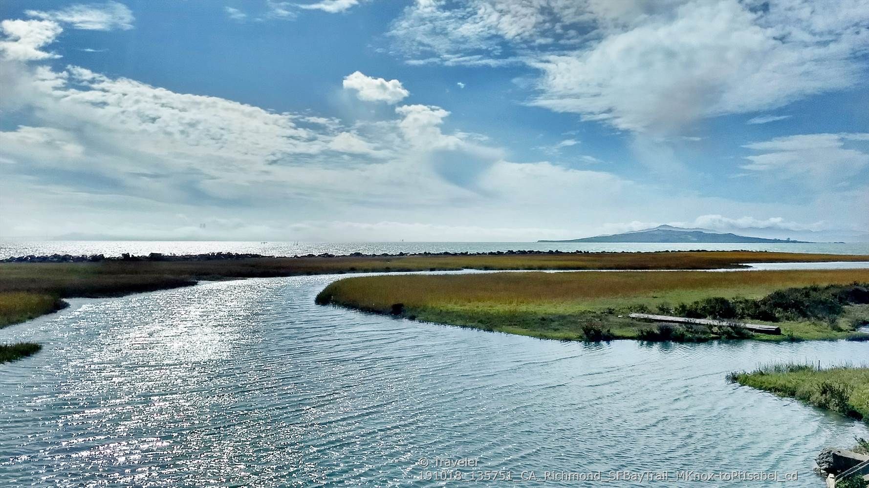 Wide river flowing through marshland under a partly cloudy sky. - San Francisco Bay Trail