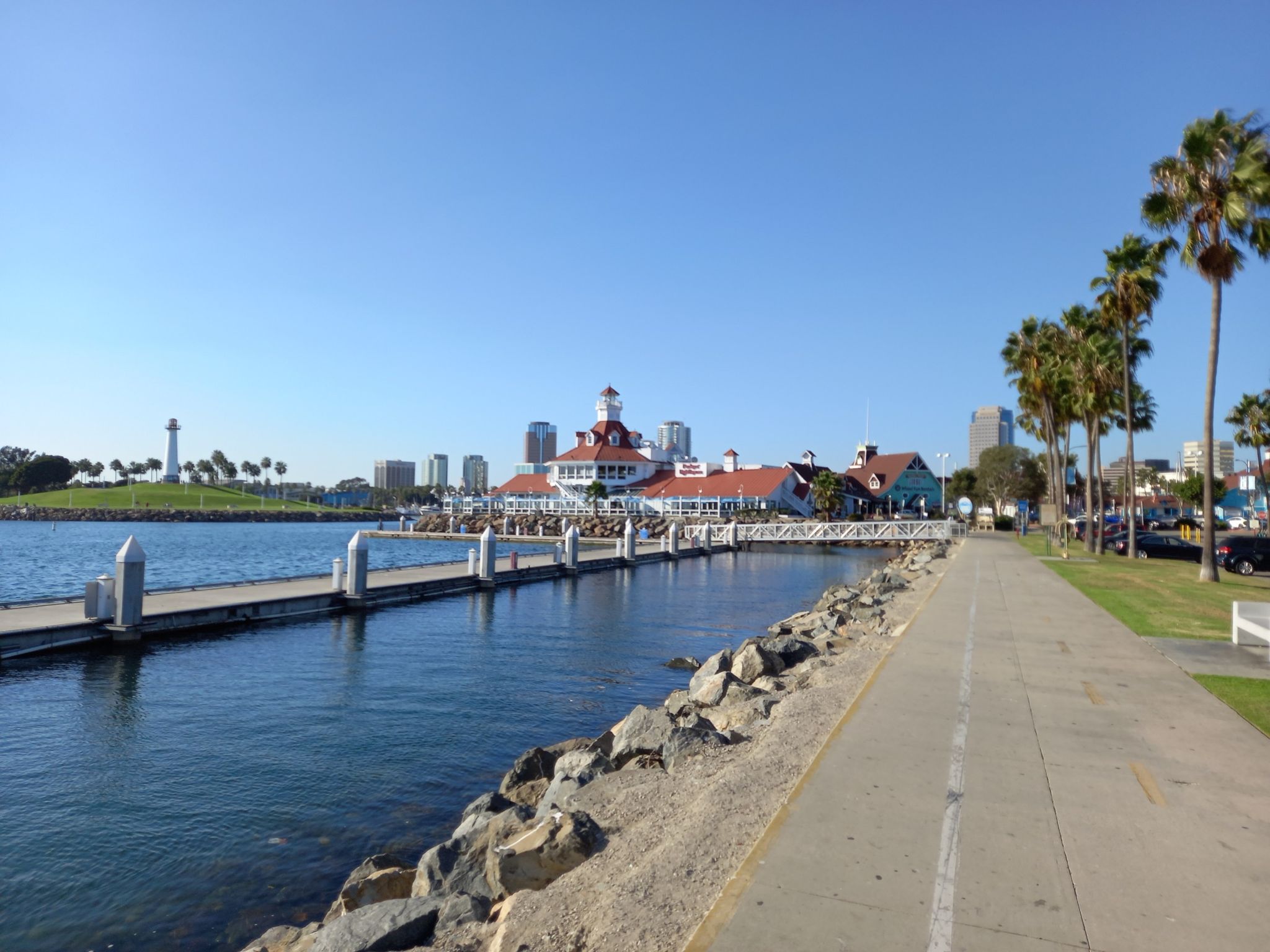 Sunny marina with a large building, palm trees, and a paved waterfront path. - Shoreline Beach Bike Path