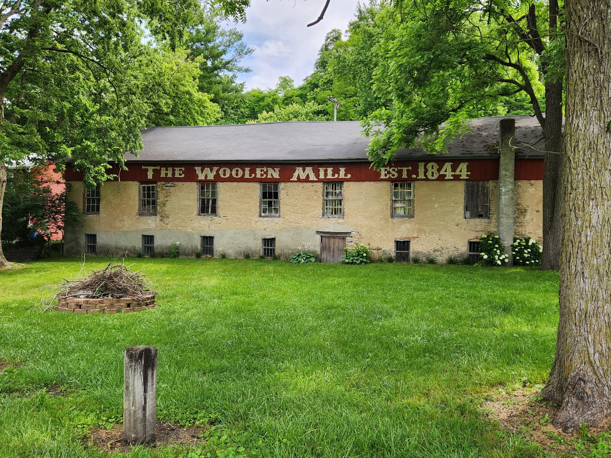 Old building with 'The Woolen Mill' sign, surrounded by green trees. - Little Miami Scenic Trail: Hedges to Founder's Park