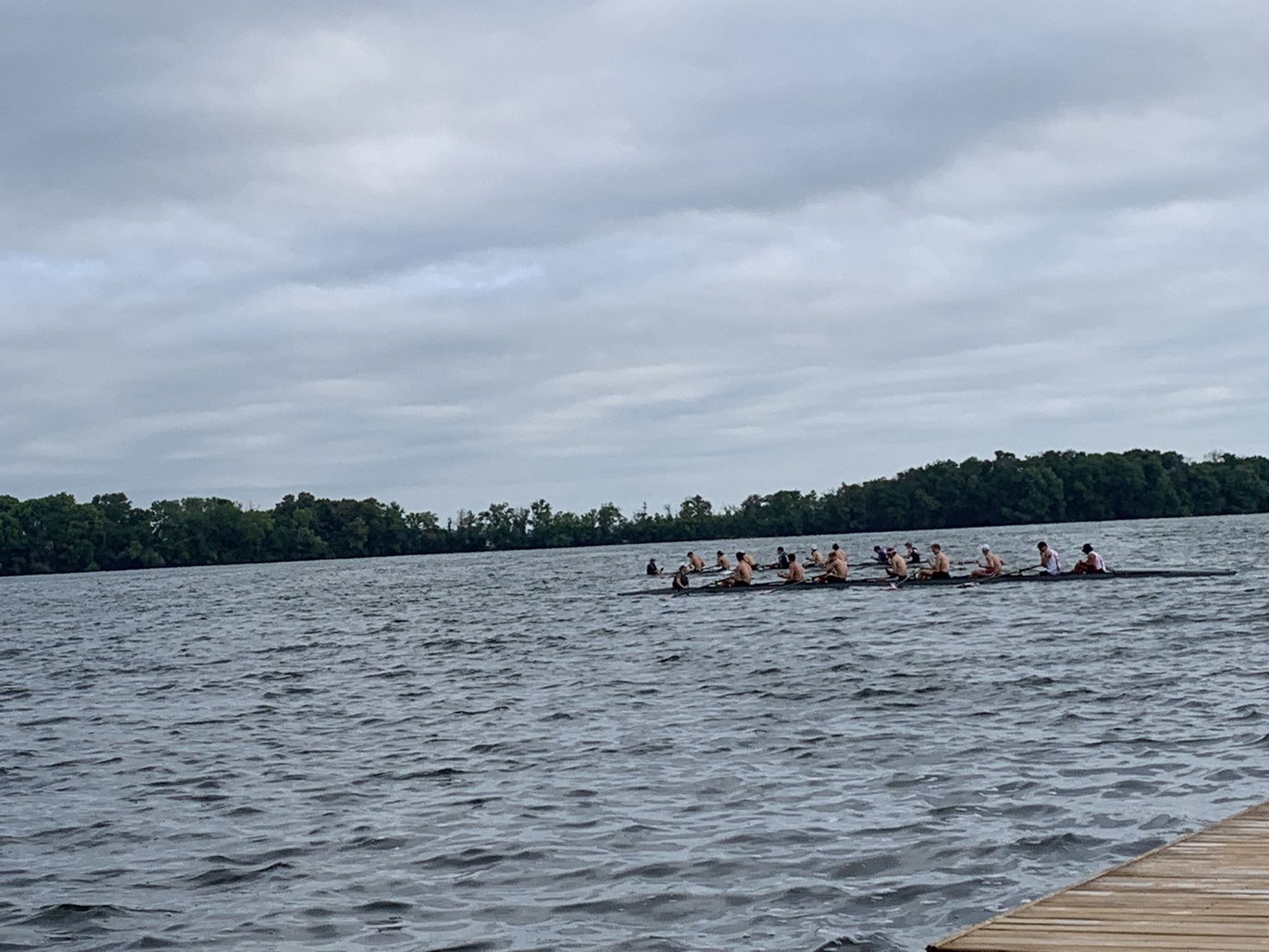Rowers in a long boat on a wide lake under a cloudy sky. - Porter Boathouse – UW–Madison Carillon Tower loop from Madison