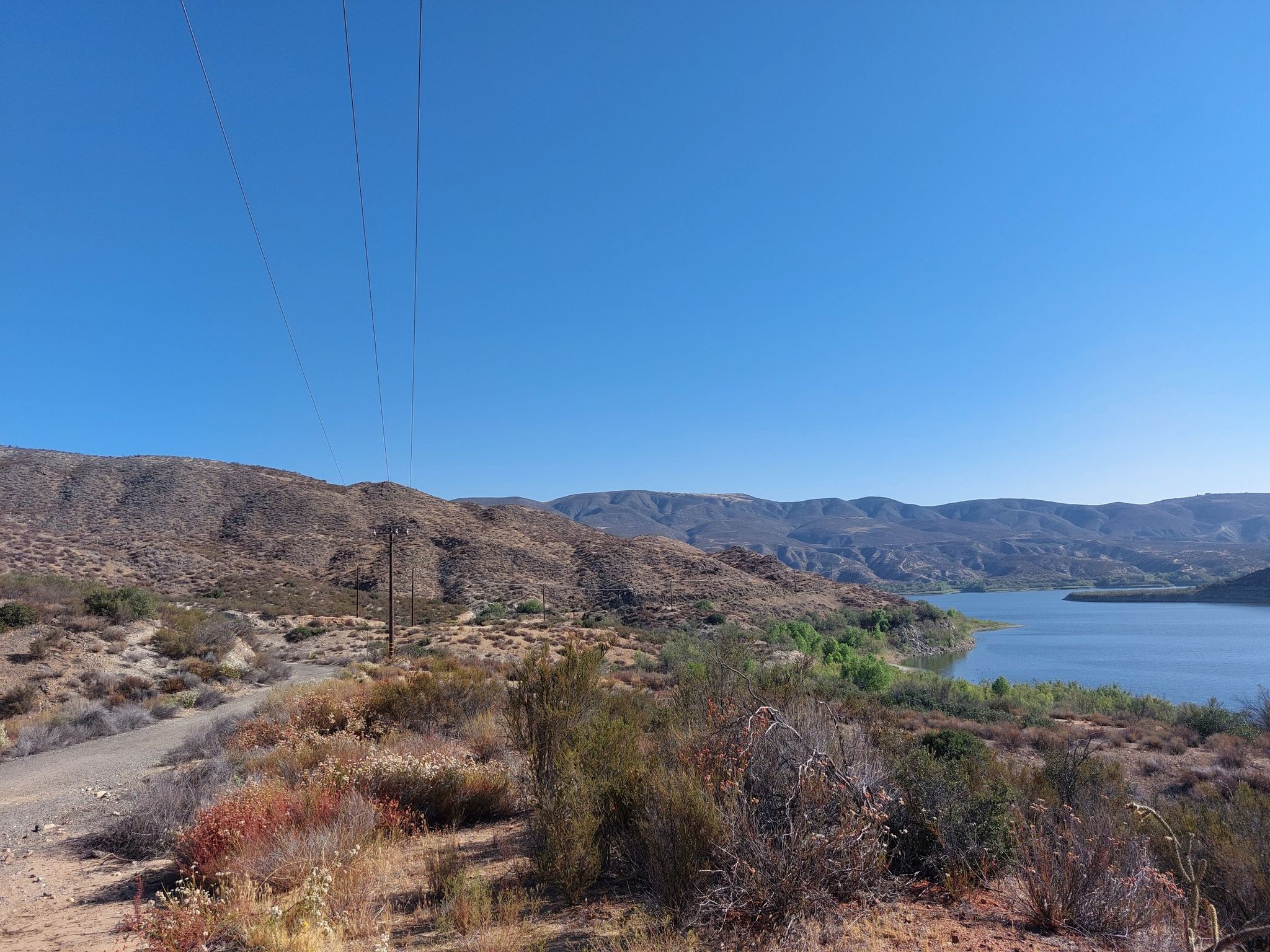 Dirt road alongside a lake, with power lines and distant mountains. - Vail Lake – Vail Lake loop from Galway Downs