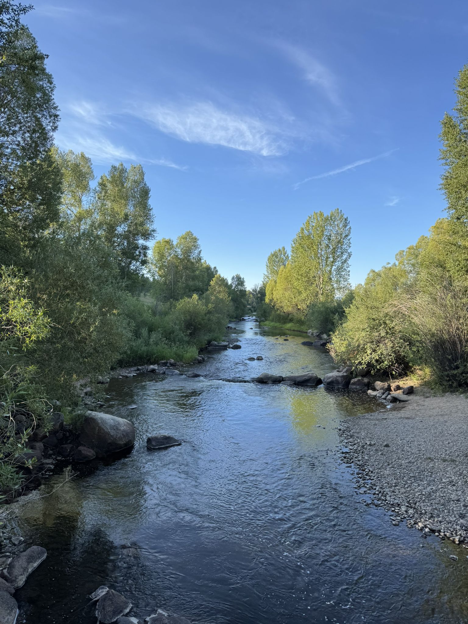 River flows through a vibrant green landscape under a clear blue sky. - Emerald Mountain loop