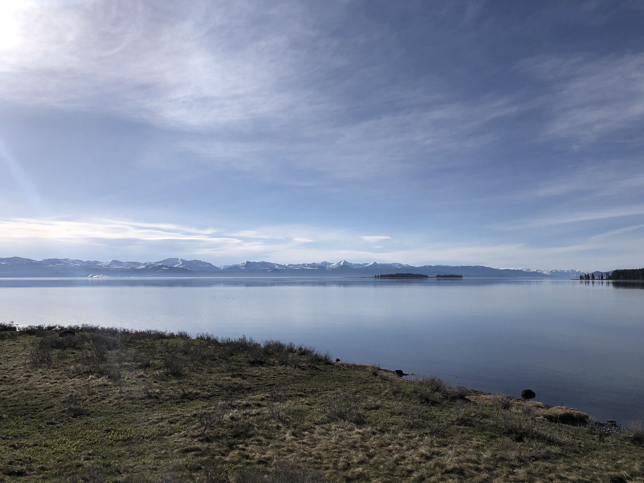 Calm lake with distant snow-capped mountains under a bright, cloudy sky. - Old Lake Road and Natural Bridge Trail
