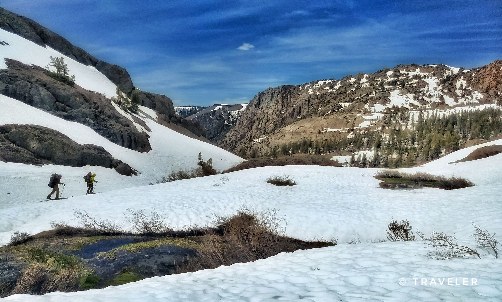 Two hikers ascend a snowy mountain valley under a bright blue sky. - Blue Canyon Trail