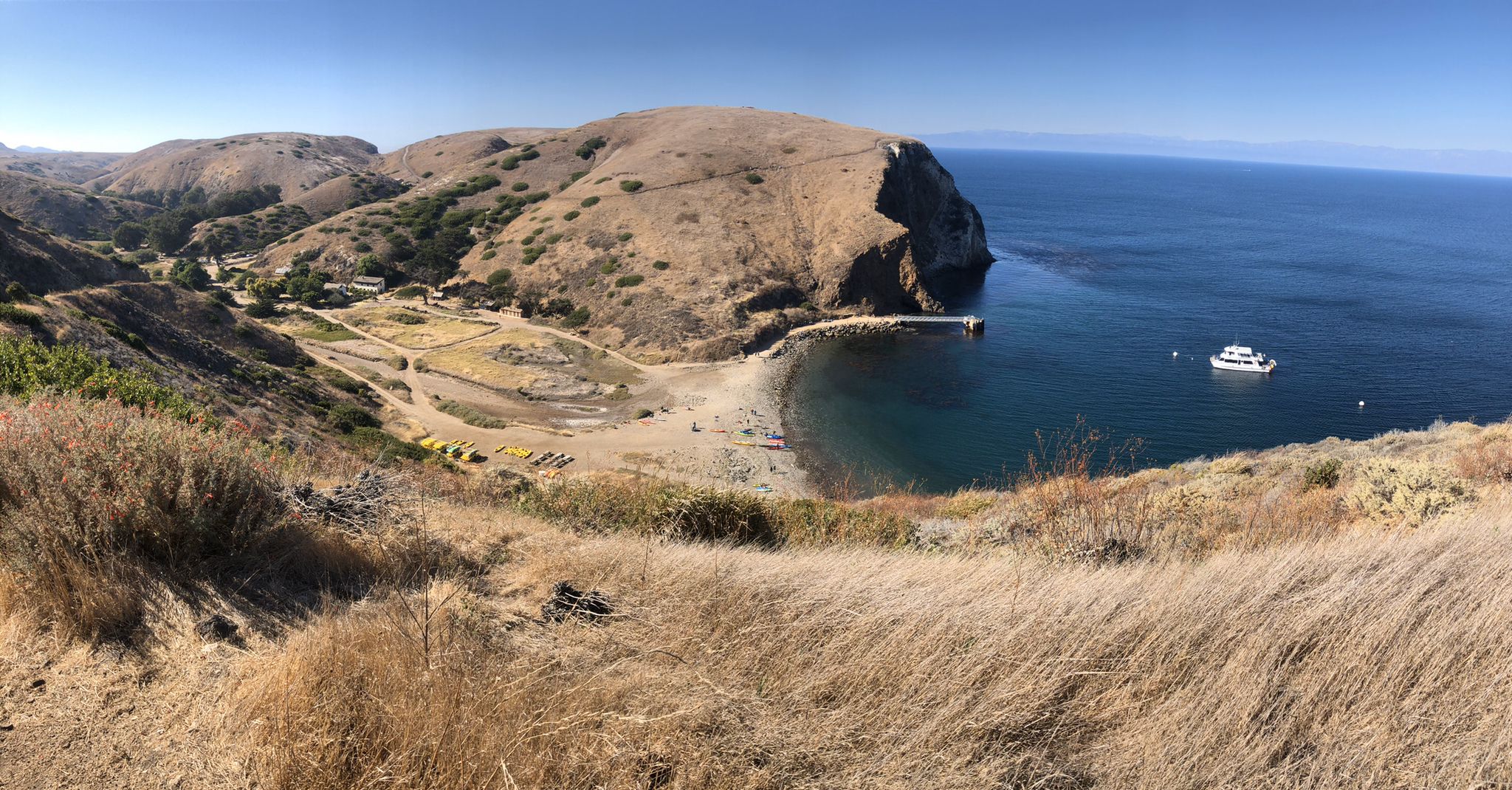 Panoramic view of a sunny bay with dry hills, a pier, and a boat. - Scorpion Canyon Loop Trail