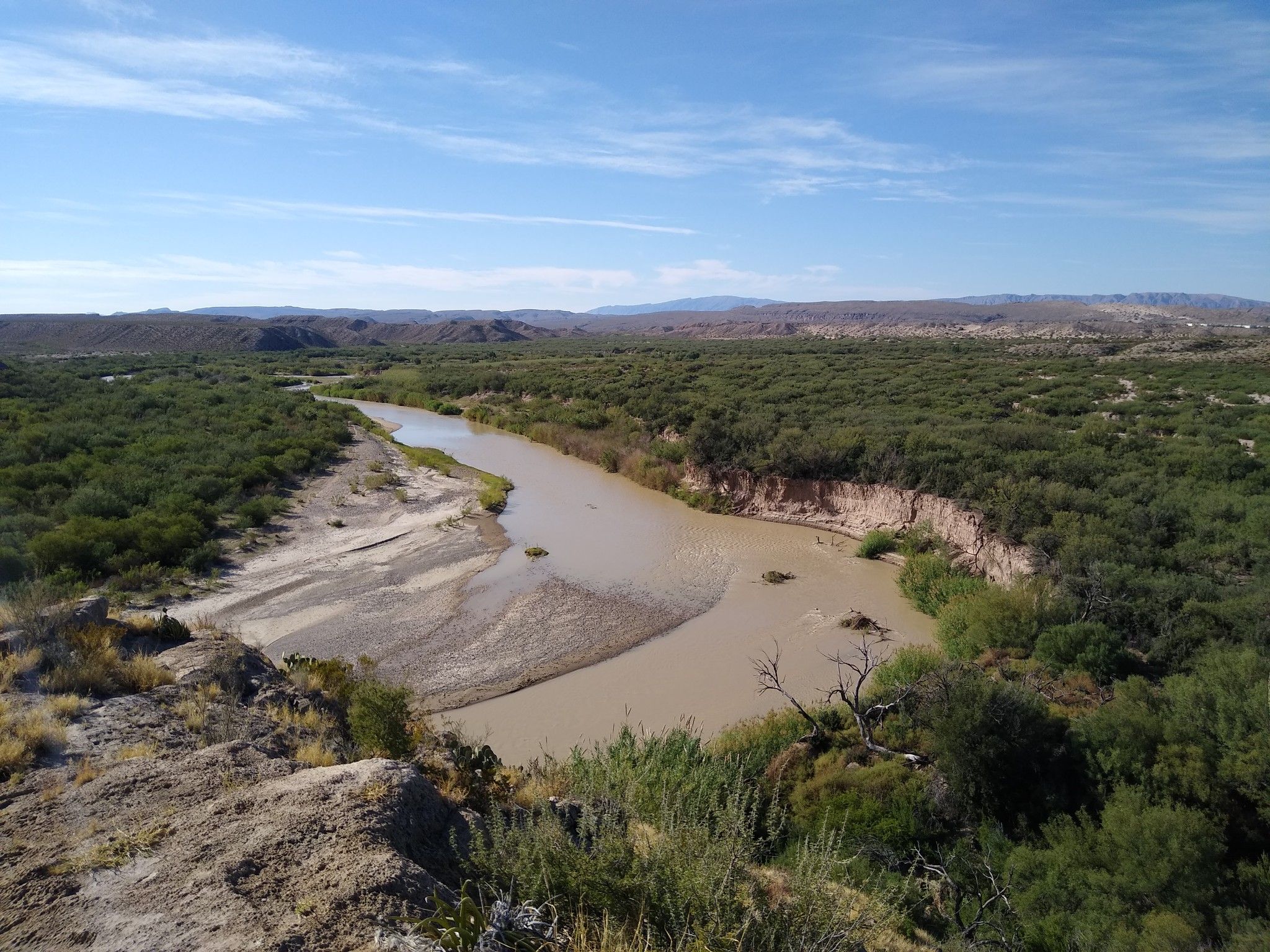 A wide, winding river flows through a green, arid landscape under blue sky. - Boquillas Canyon Trail