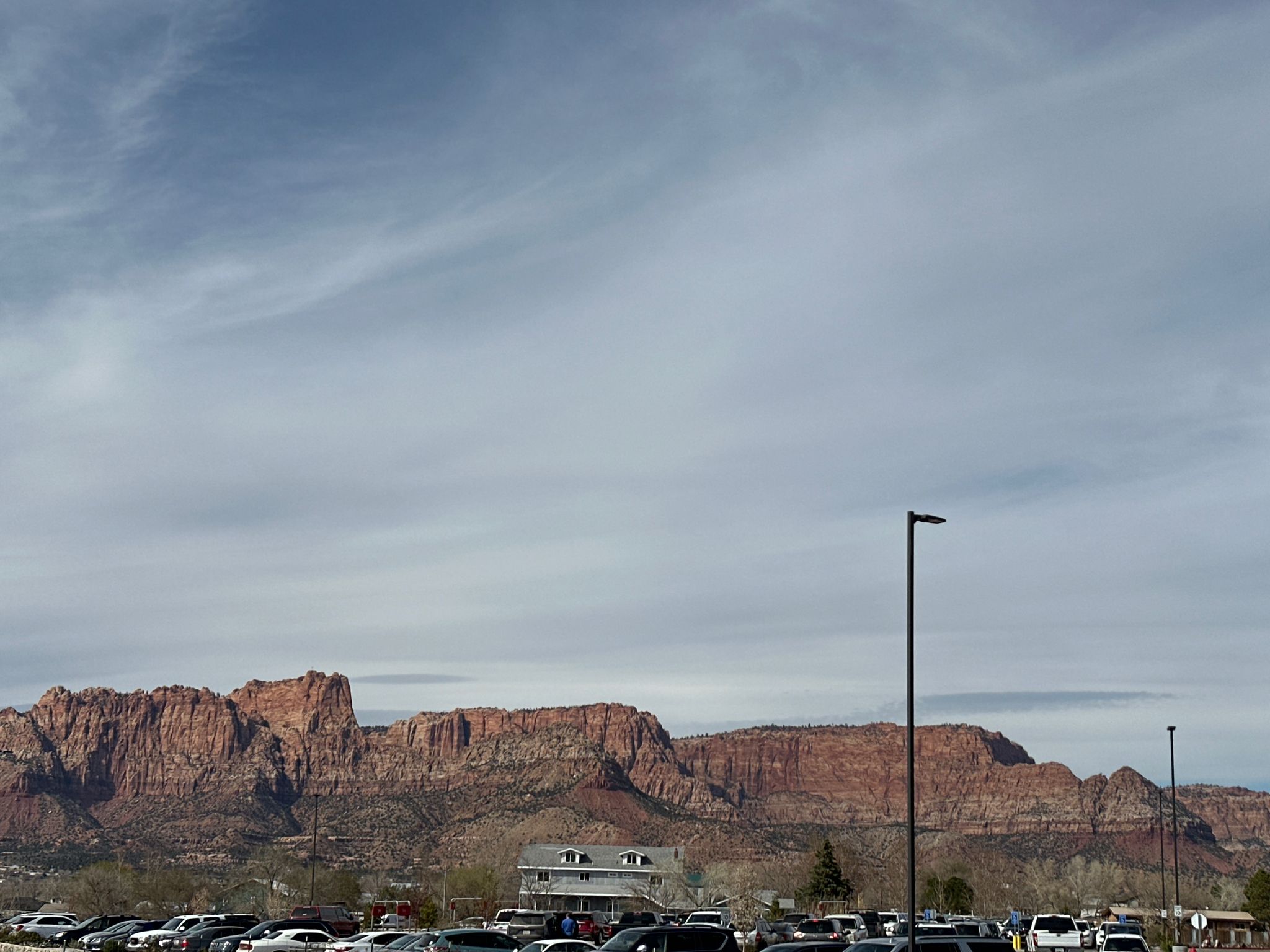 Red rock mountains loom over a parking lot and buildings under cloudy skies. - Colorado City loop