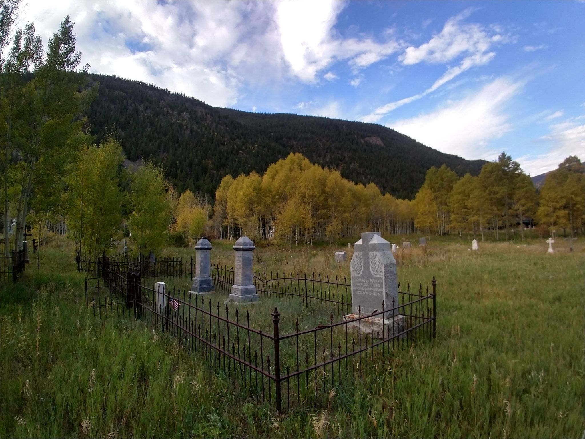 Cemetery with fenced gravestones, golden aspens, and dark mountains under a bright sky. - Clear Creek Greenway