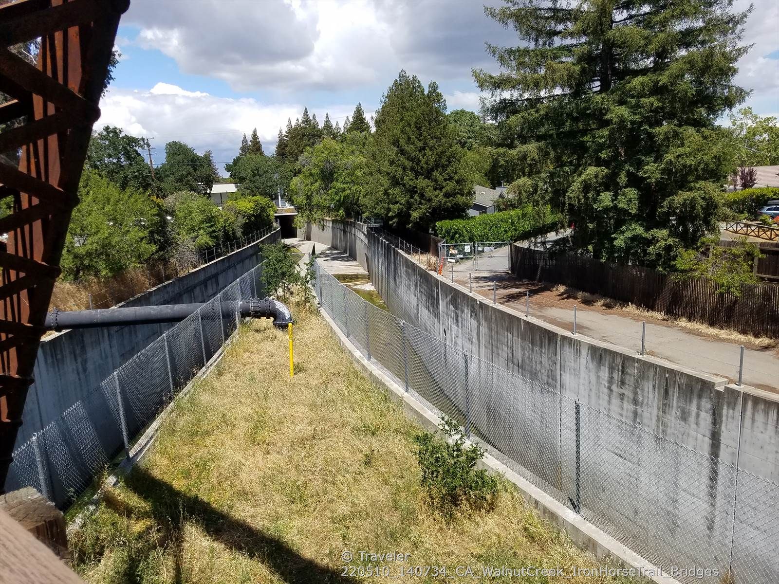 Overlooking a concrete channel with fences, surrounded by green trees. - Iron Horse Regional Trail