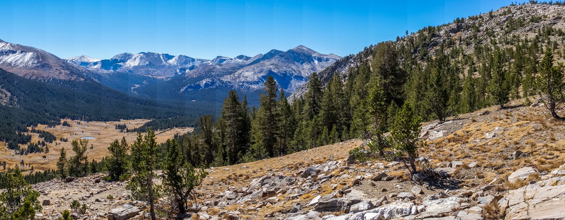 Panoramic view of a vast mountain valley with forests and snow-capped peaks. - Gaylor Lakes Trail
