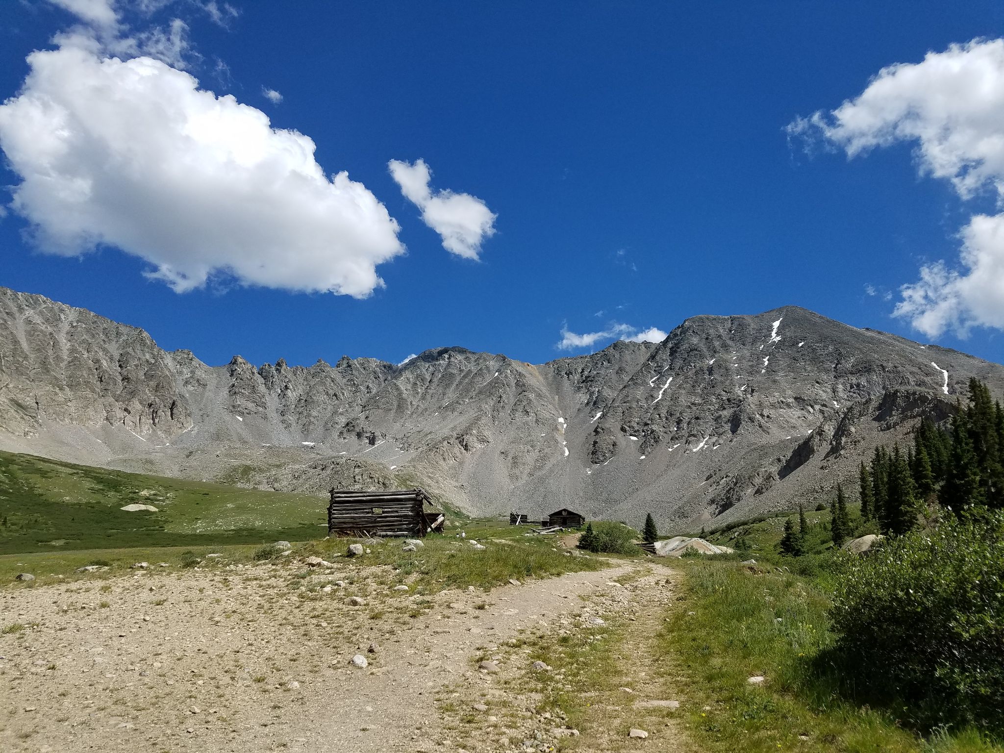 Historic wooden cabins in a vast mountain valley under a bright blue sky. - Mayflower Gulch Trail