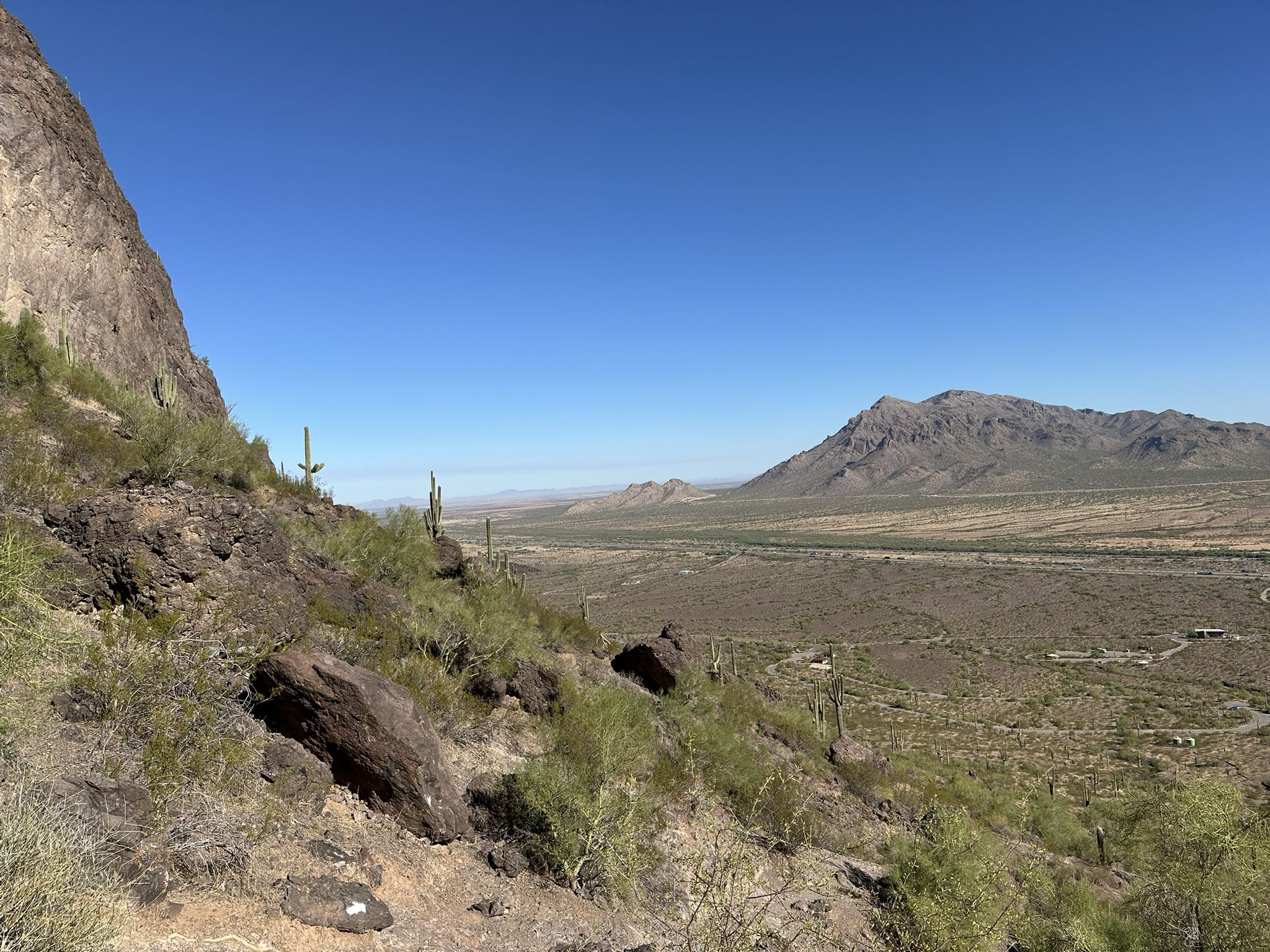 Expansive desert valley with rocky slopes, distant mountains, and clear blue sky. - Hunter Trail