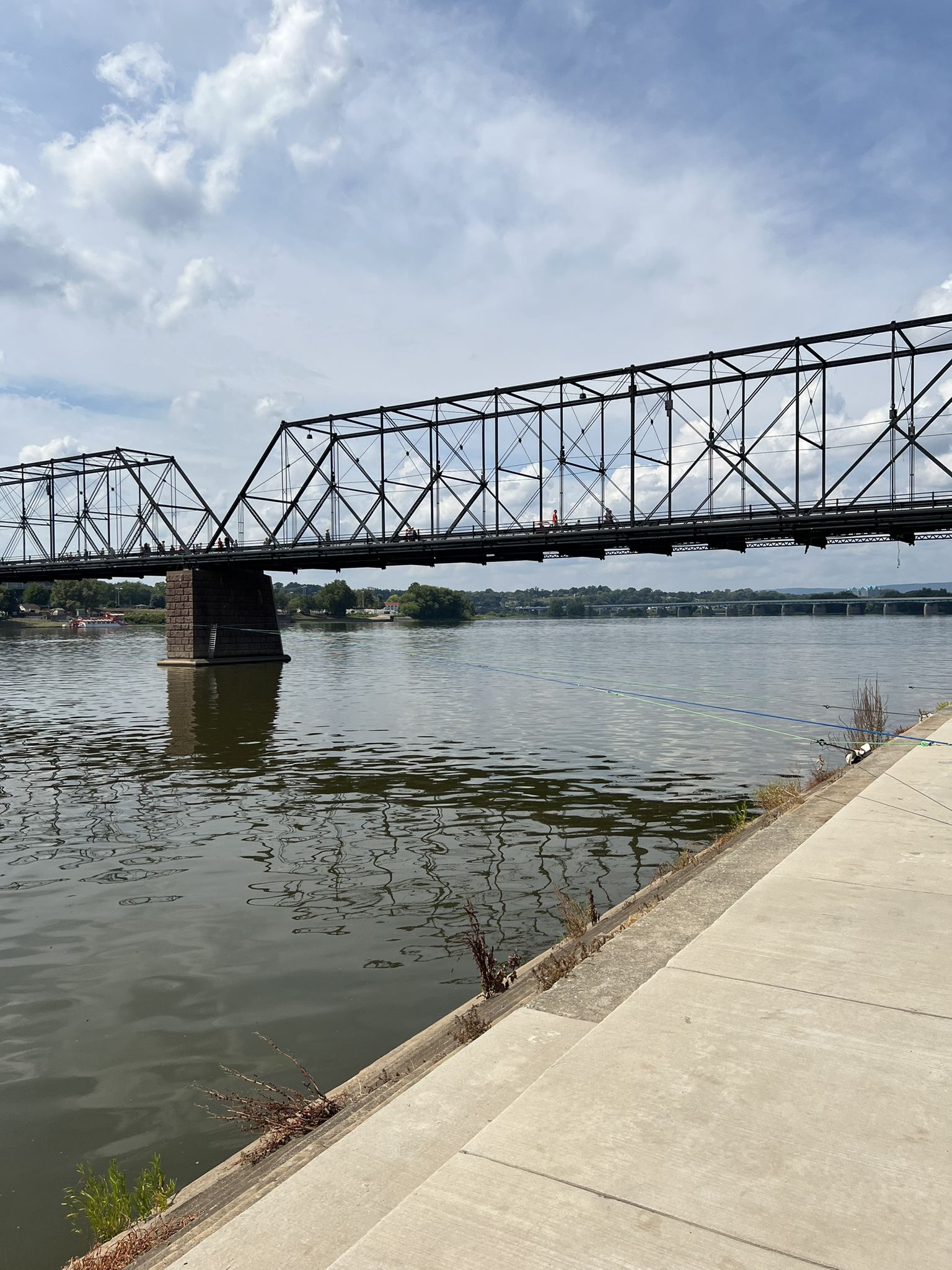 A large metal truss bridge spans a wide river under a cloudy sky. - Capital Area Greenbelt Trail