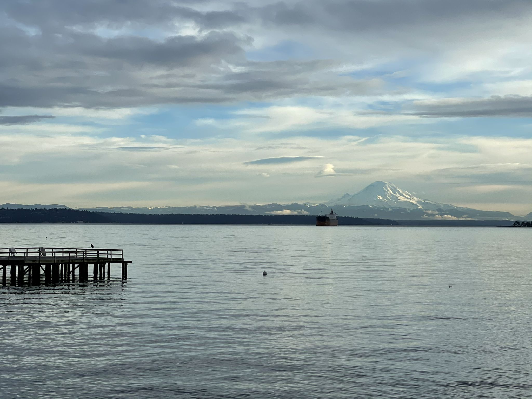 Wooden pier in calm water, with a distant snow-capped mountain under cloudy sky. - Cascadia Marine Trail – Battery Vinton loop from Fort Ward Park