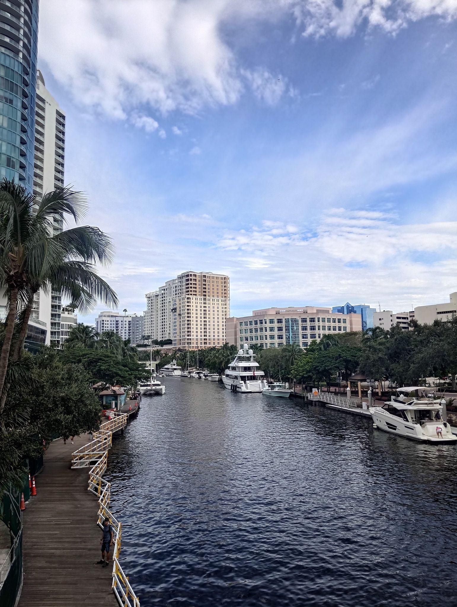 River with boats and tall buildings, a person on a wooden walkway. - Fort Lauderdale Riverwalk