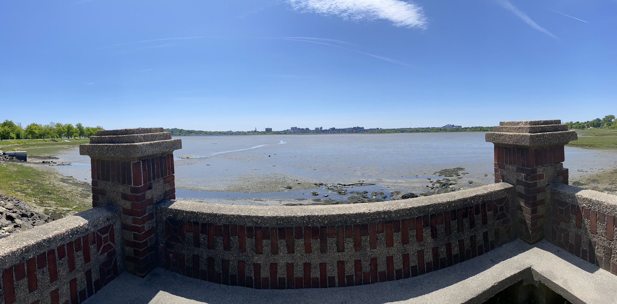 A panoramic view of a bay from a brick wall, with distant land under a sunny sky. - Back Cove Trail – Canco Woods loop from Portland