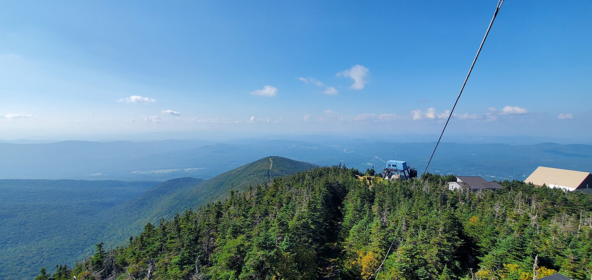 Mountain peak with buildings and a cable, overlooking distant hazy mountains. - Cannon Mountain via Kinsman Ridge Trail