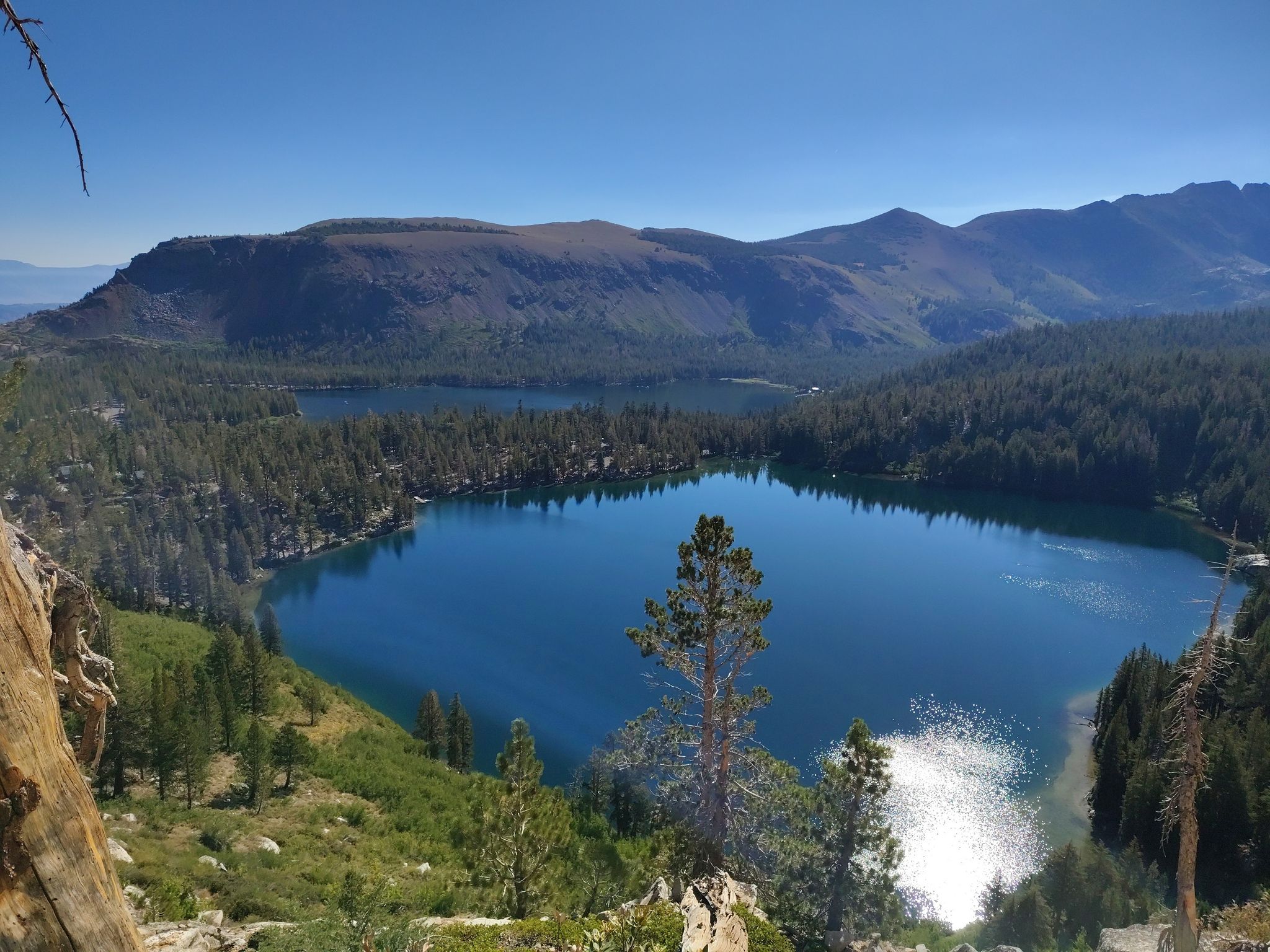 Two clear blue lakes nestled among green forests under a bright sky. - Lakes Basin Loop