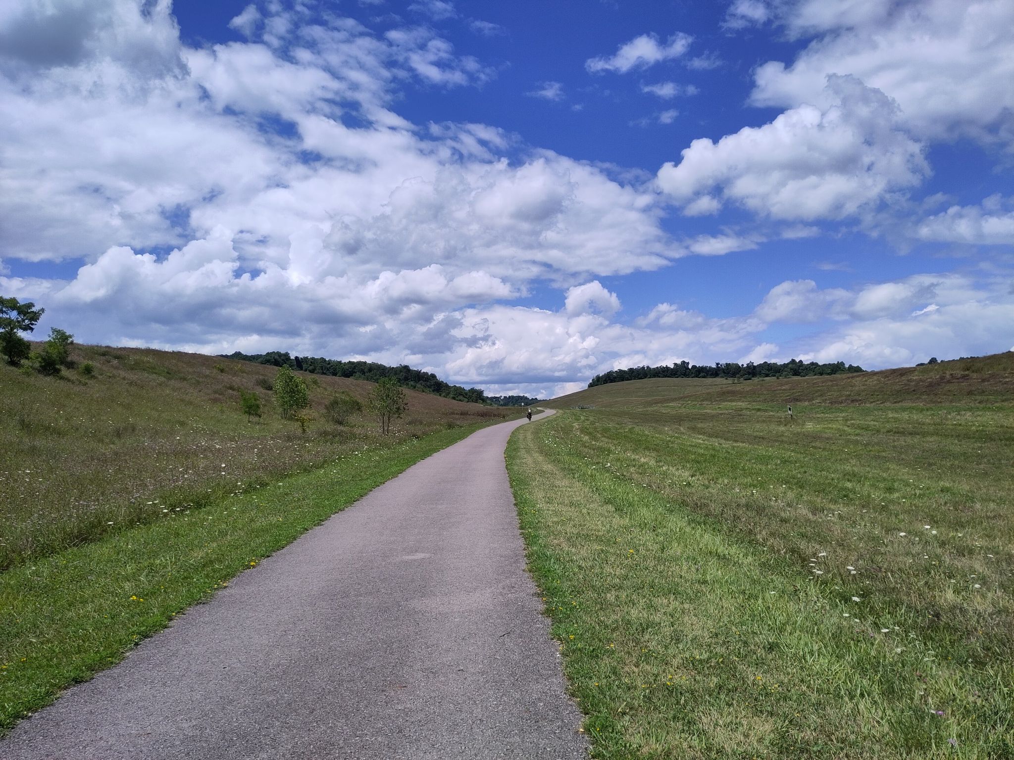 Paved path through green, rolling hills under a blue, cloudy sky. - Roadbike loop from Weirton
