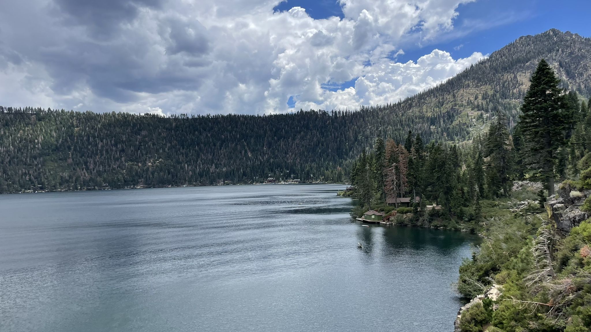 Wide lake with forested mountains and a building on the shore under a cloudy sky. - Cathedral Lake via Mount Tallac Trail
