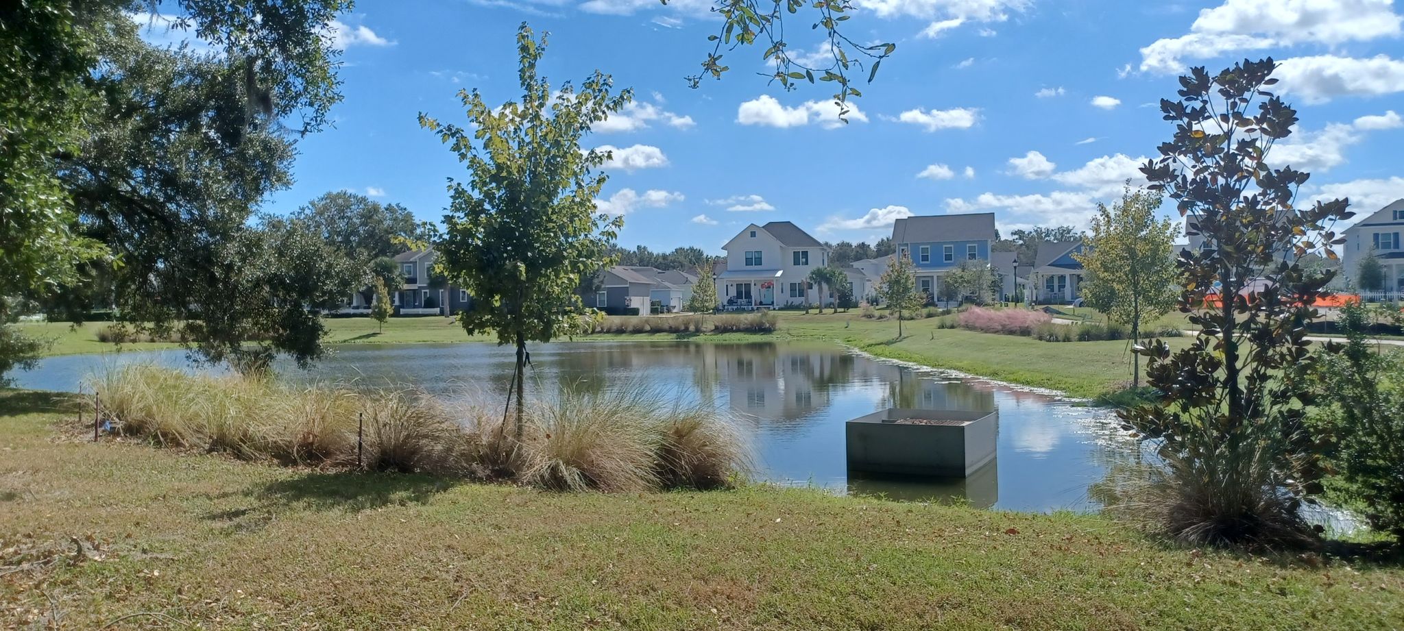 A calm pond reflecting houses under a bright blue sky with clouds. - West Orange Trail – Downtown Winter Garden loop from Winter Garden