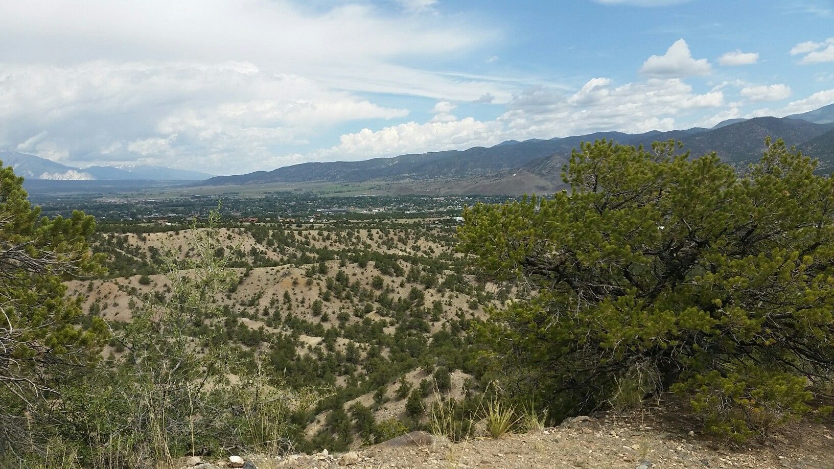 Panoramic view of arid hills, a green valley, and distant mountains under cloudy skies. - Racetrack and Lost Trails loop