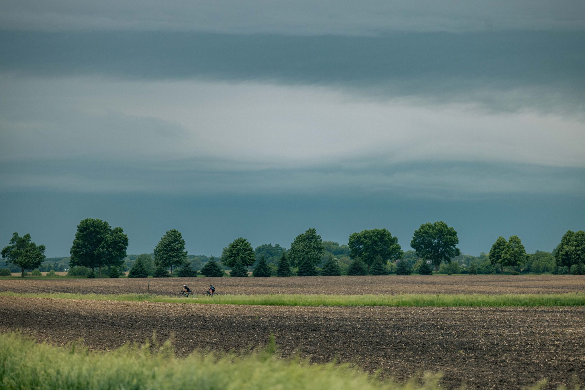 Two cyclists ride across a wide field under a cloudy, overcast sky. - Lake Highland loop from Grand Prairie