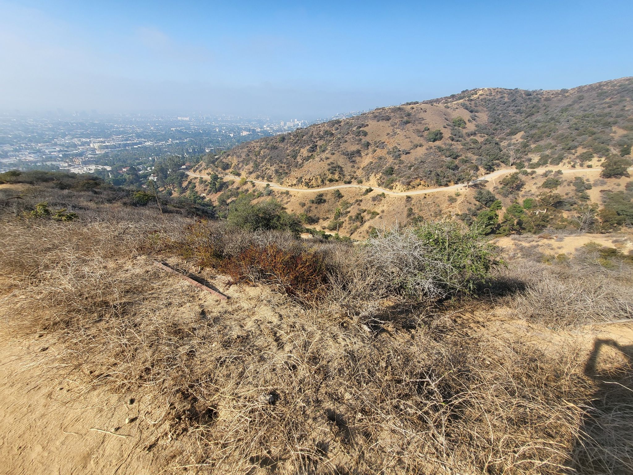 Dry, brush-covered hillsides with a winding dirt path and hazy city in distance. - Inspiration Point – Runyon Canyon Park