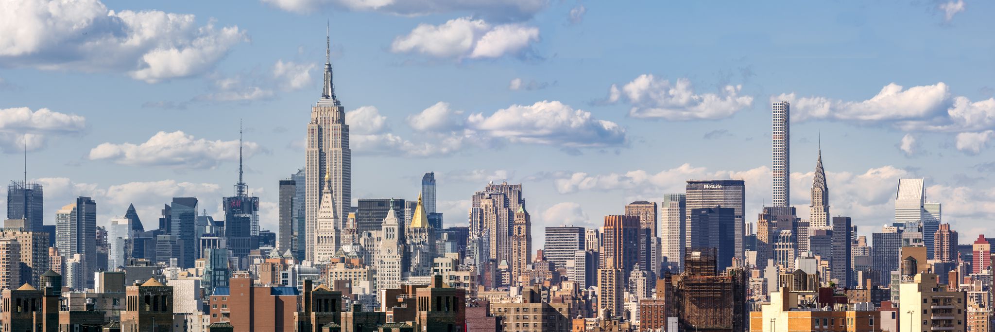Panoramic view of a dense city skyline with many skyscrapers under a cloudy sky. - Brooklyn Bridge Walk