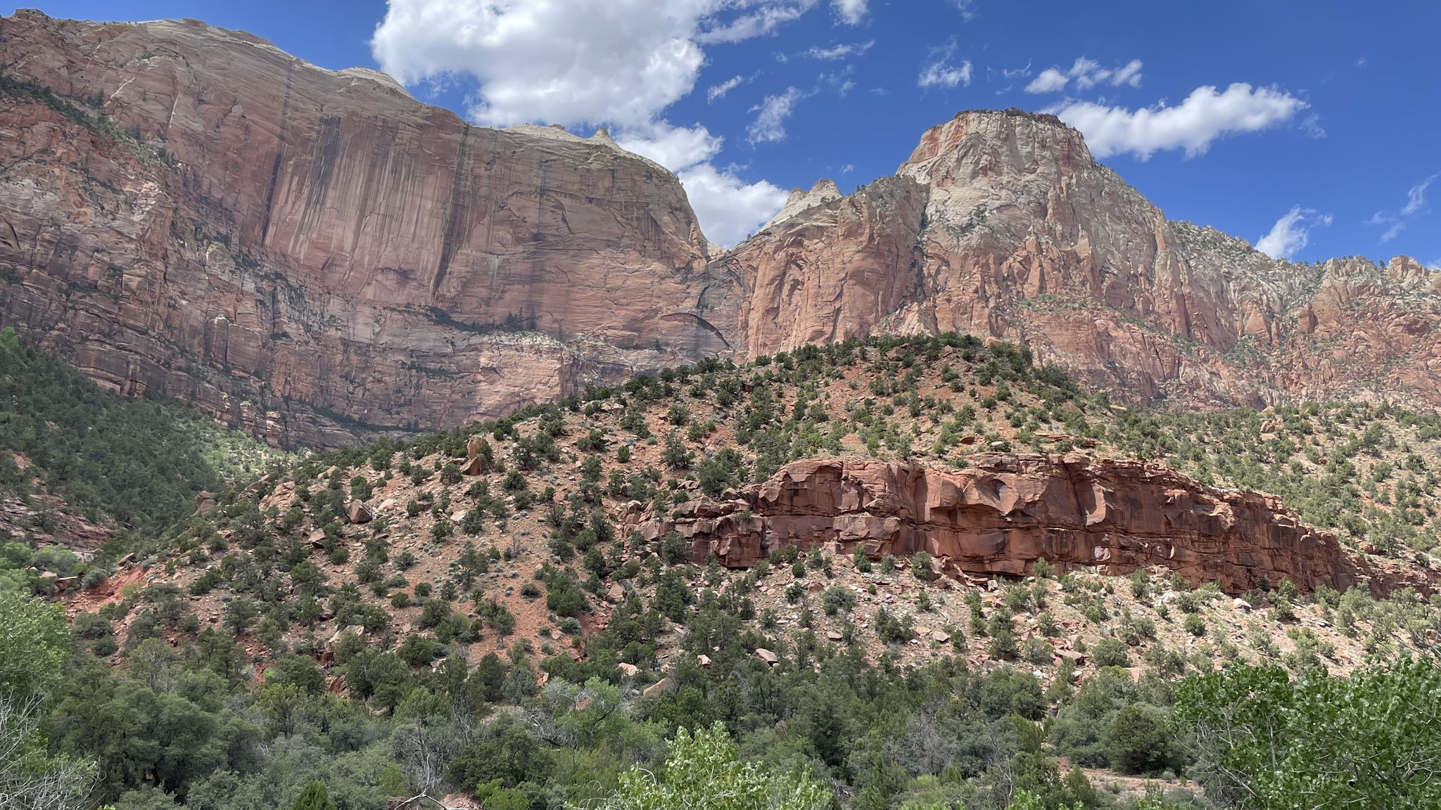 Towering red and white rock formations rise above scrub-covered hills under a blue sky. - Zion—Mount Carmel Highway – Zion–Mount Carmel Highway loop from Zion Human History Museum