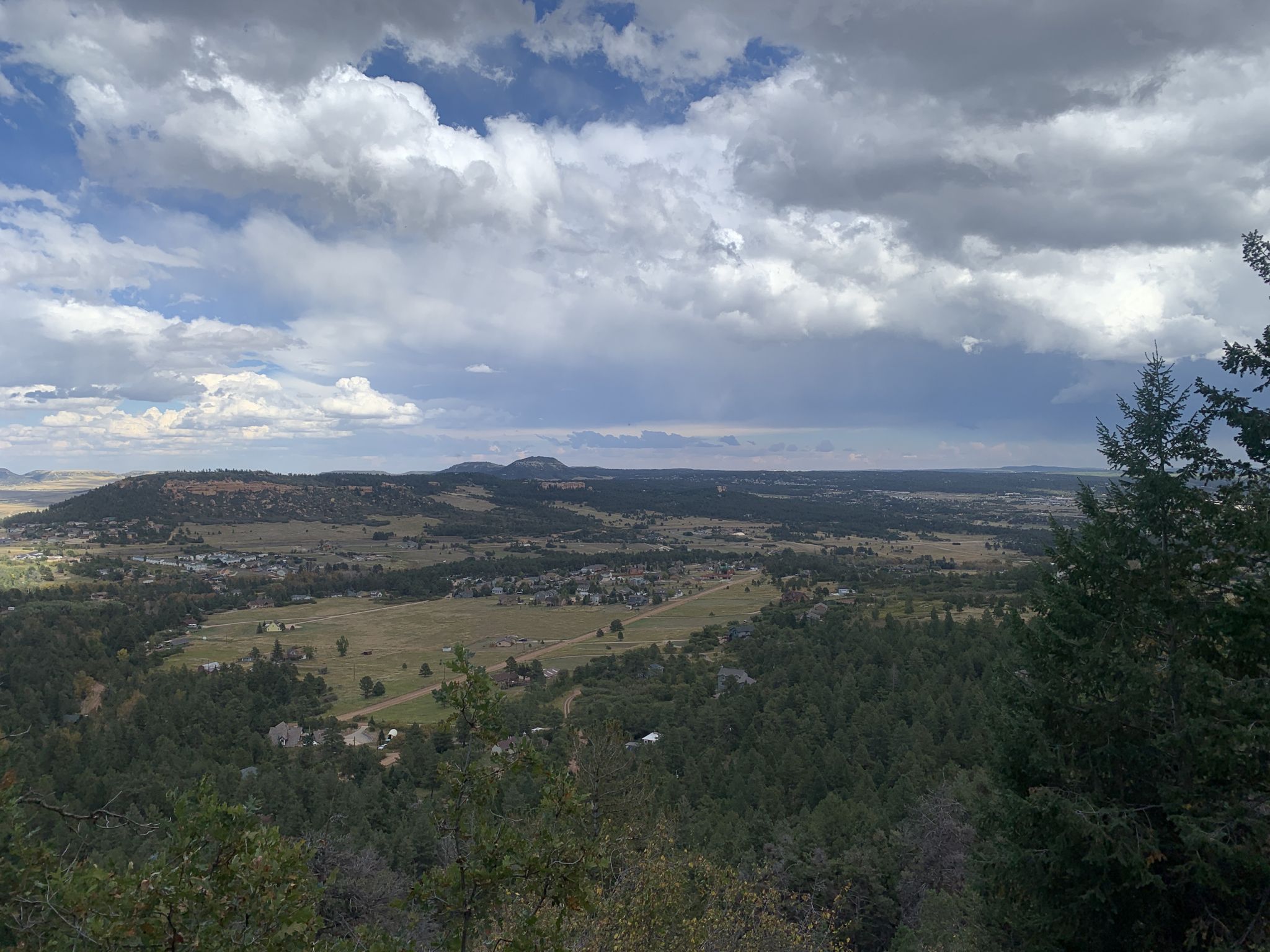An expansive view of a valley with fields, buildings, and distant hills under a cloudy sky. - Raspberry Mountain Loop