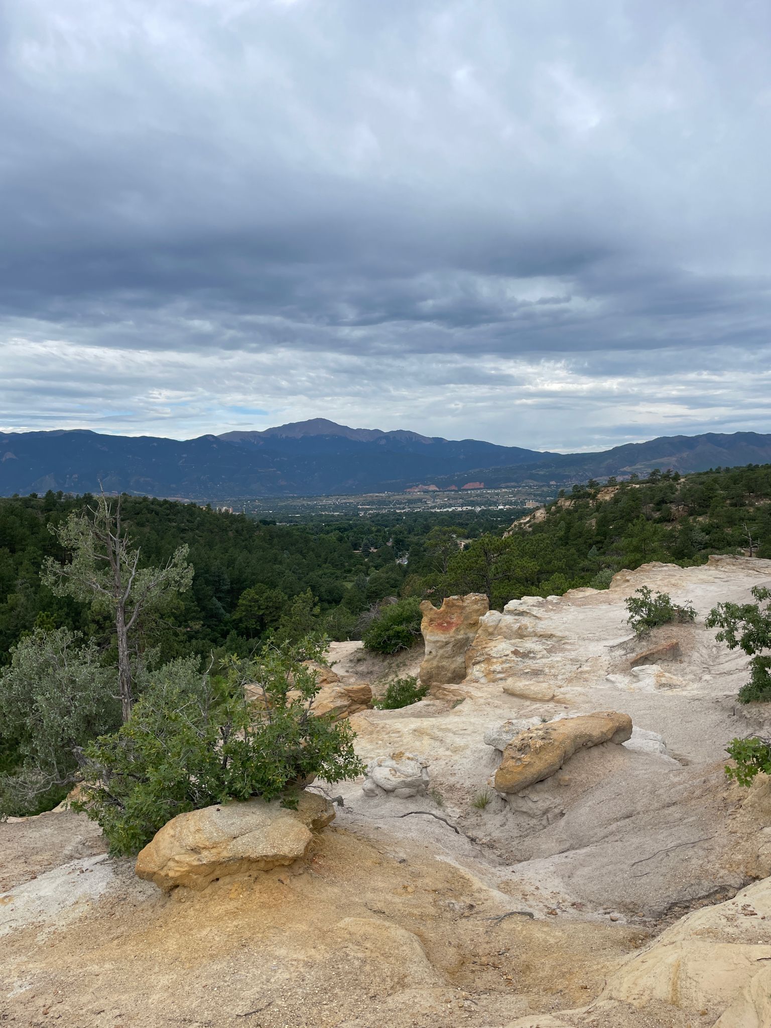 Rocky foreground overlooks a green valley and distant mountains under cloudy skies. - Palmer Park trail ride loop