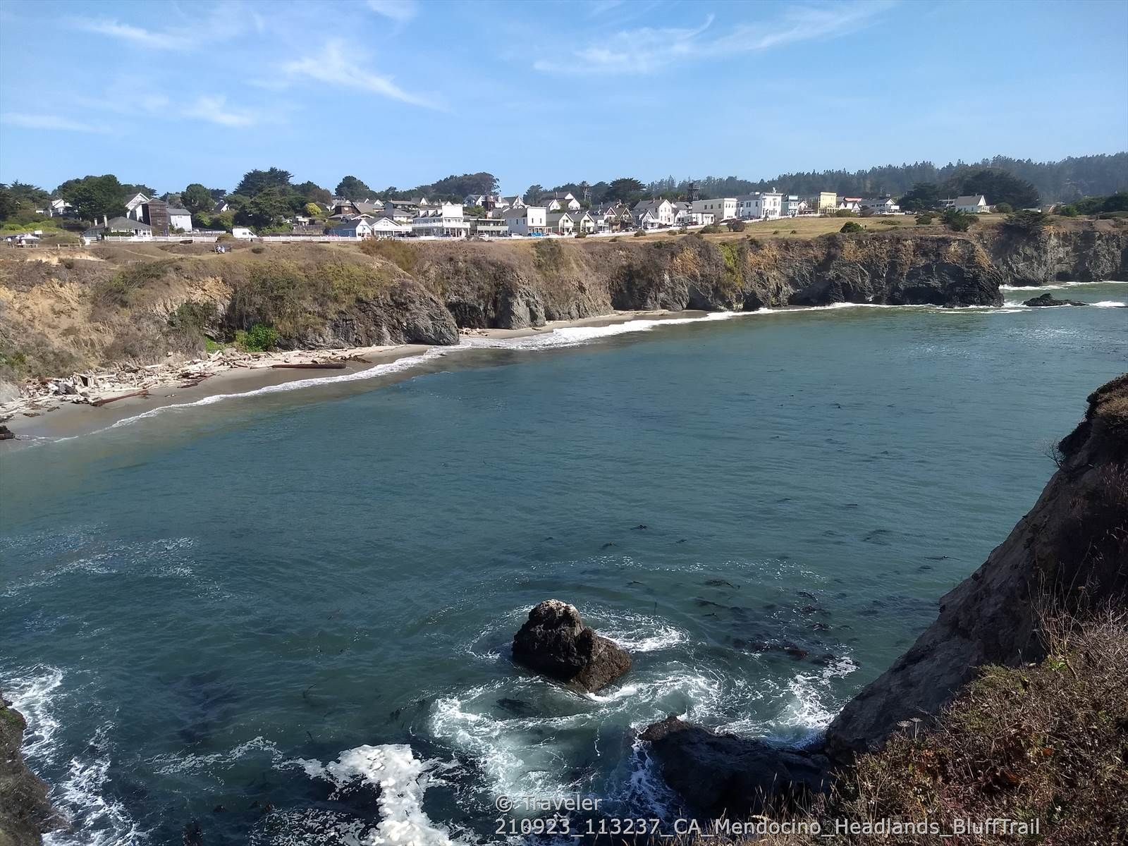 Bright coastal view of blue ocean, rocky outcrops, and distant houses on cliffs. - Mendocino Headlands Bluff Trail