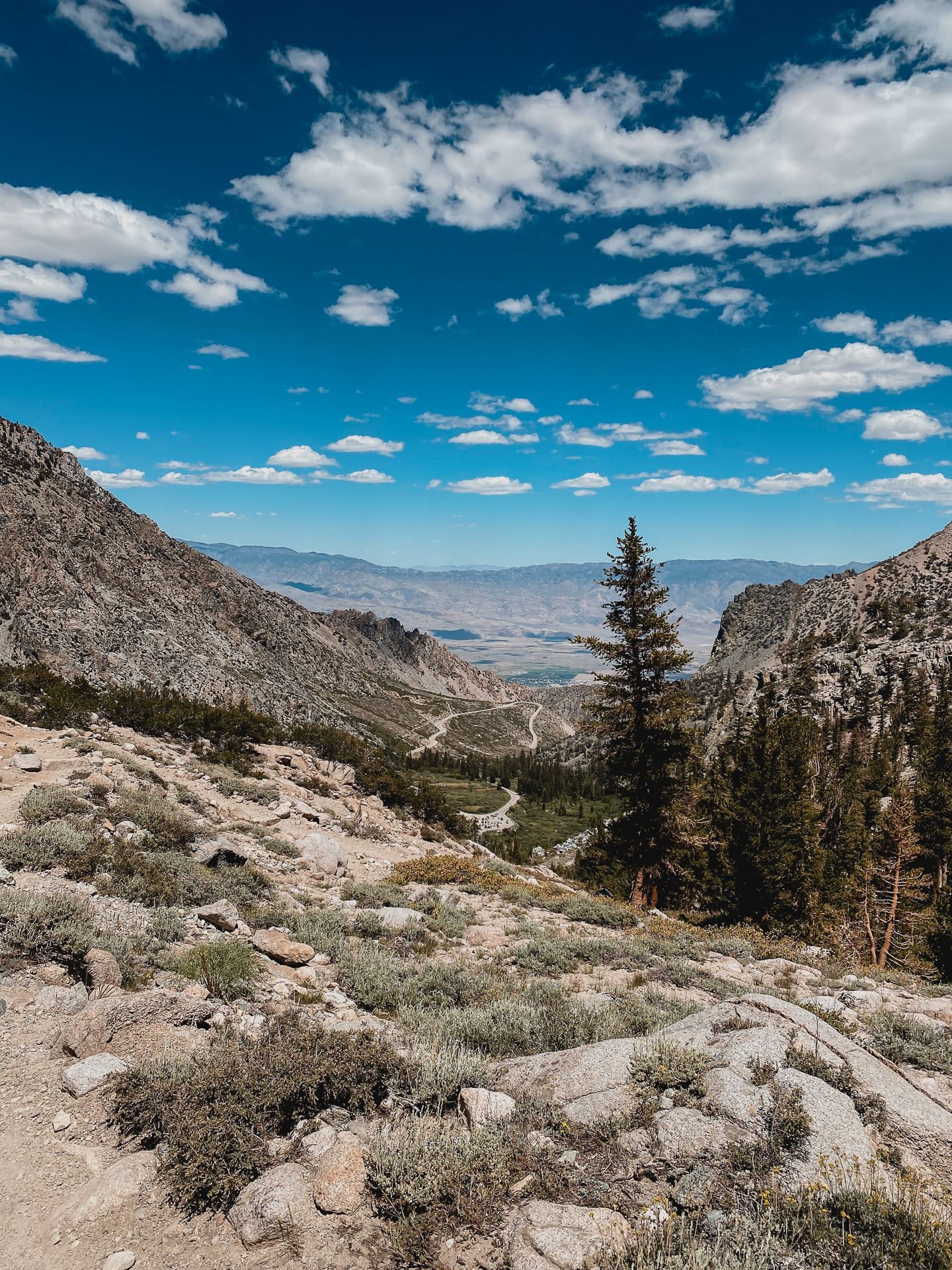 A winding road descends through a rocky mountain valley under a blue sky. - Flower Lake via Kearsarge Pass Trail