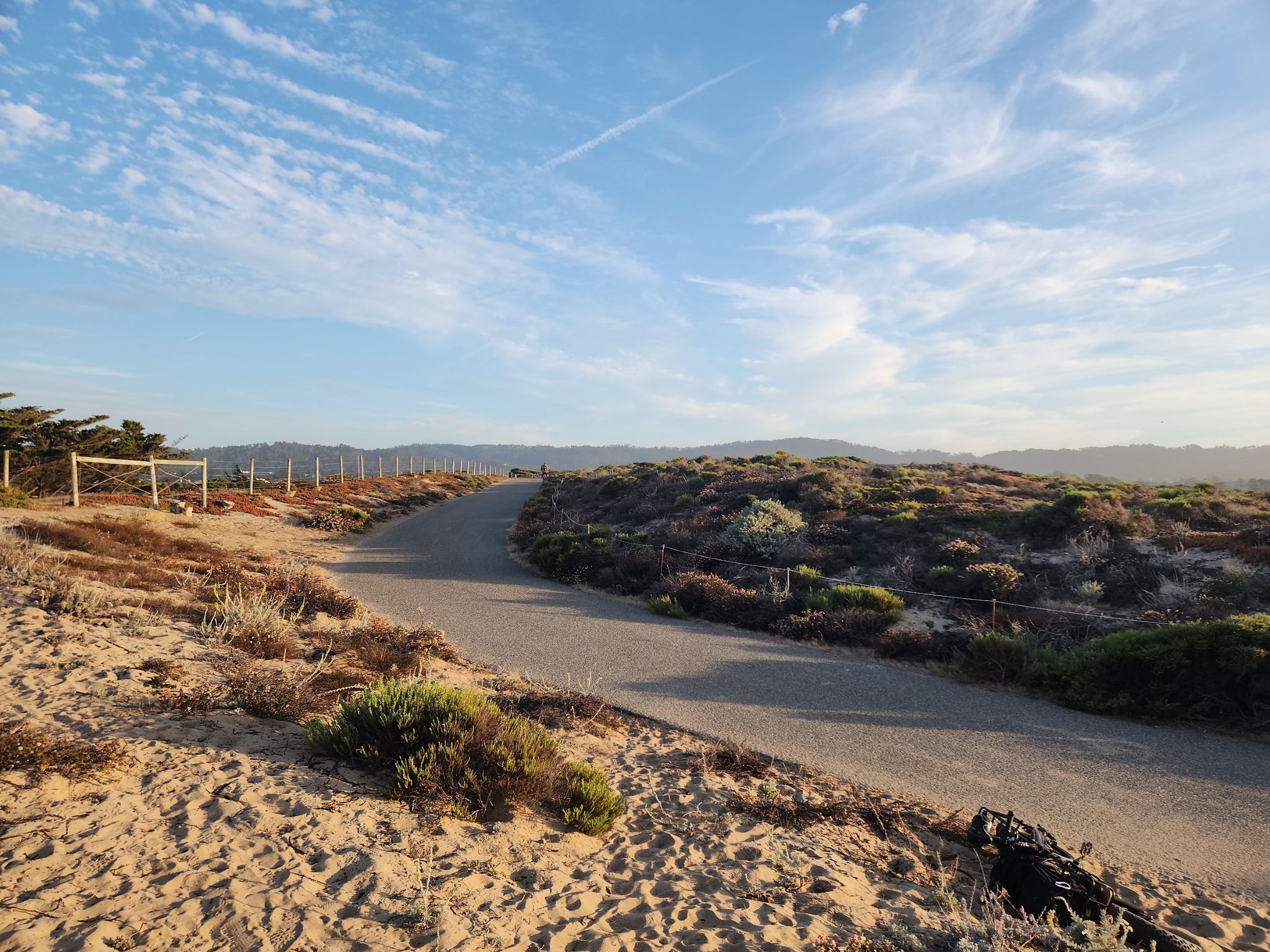Paved path curves through sandy, scrubby landscape under a bright sky. - Monterey Beach – Monterey State Beach loop from Seaside
