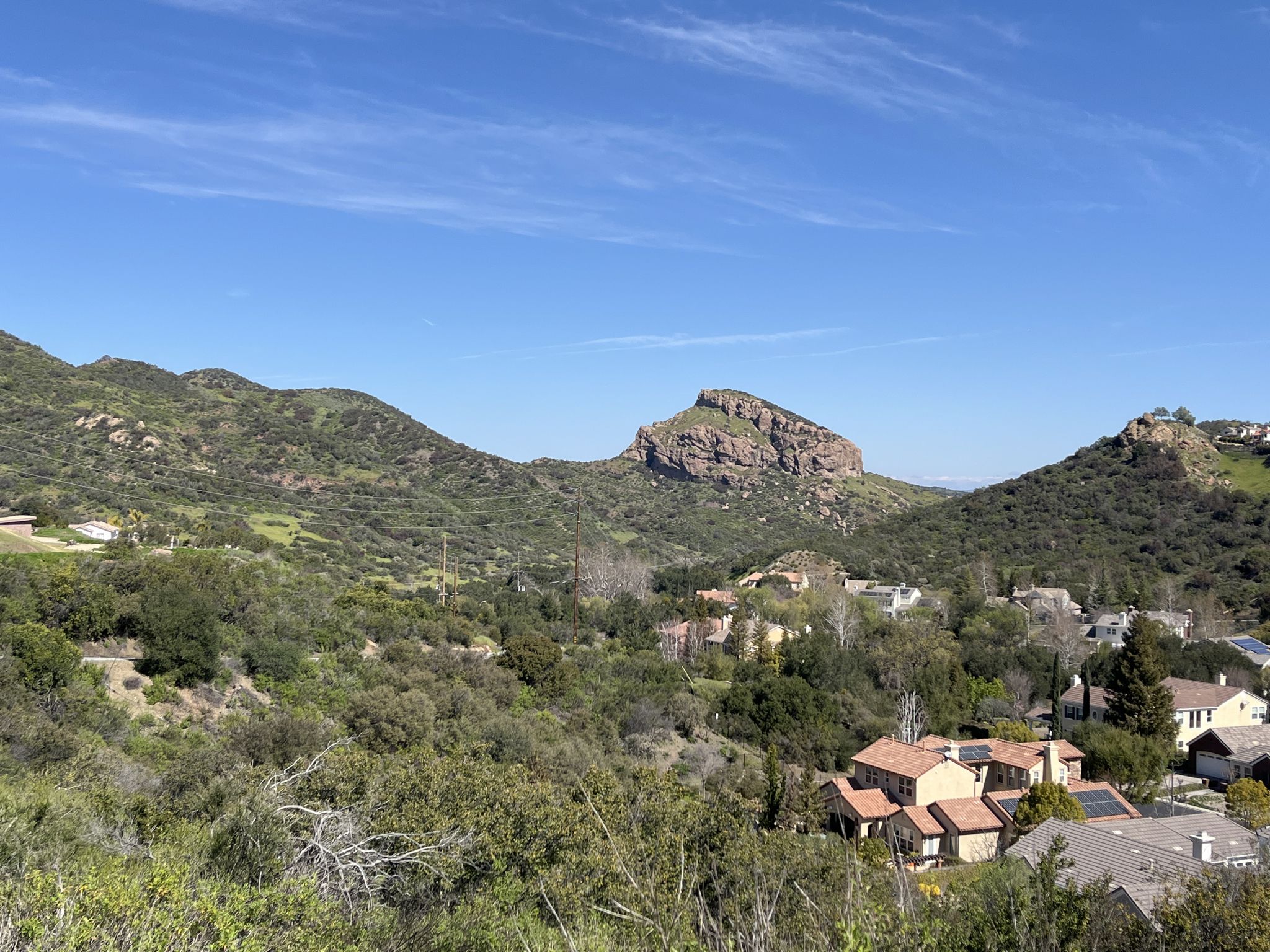 Expansive view of green hills, rocky outcrops, and scattered homes under blue sky. - Malibu Creek State Park loop