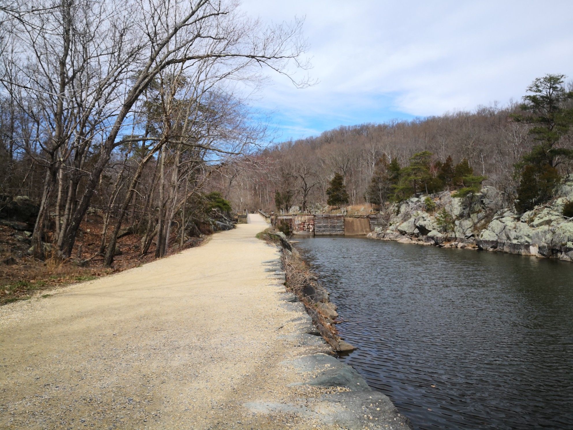 Dirt path runs alongside a calm river with bare trees and distant hills. - Billy Goat A Trail Entrance loop from Chesapeake and Ohio Canal National Historical Park