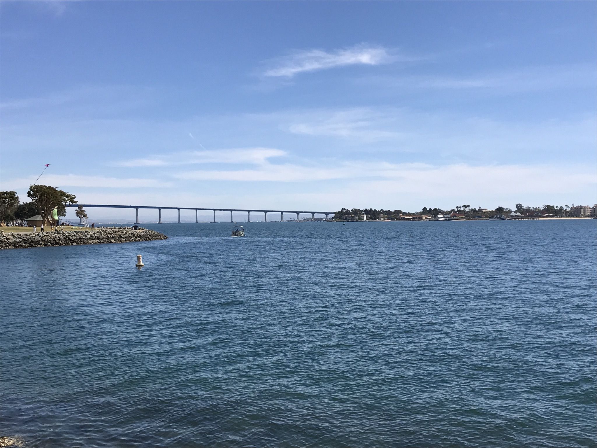 Expansive bay with a long bridge in the distance under a blue sky. - Bayshore Bikeway