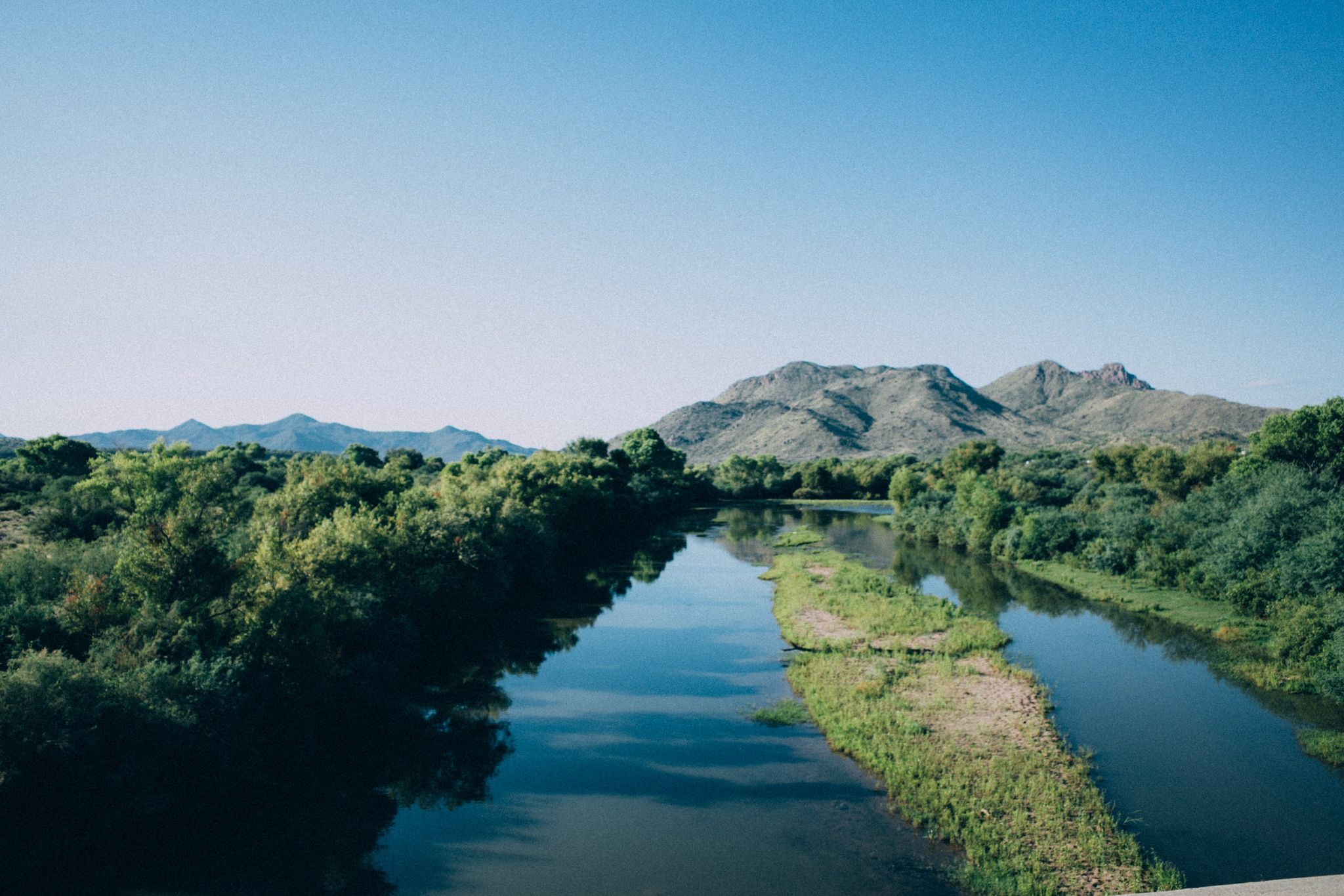 A wide river flows through green trees with distant mountains under a clear sky. - Saguaro Lake & Salt River loop