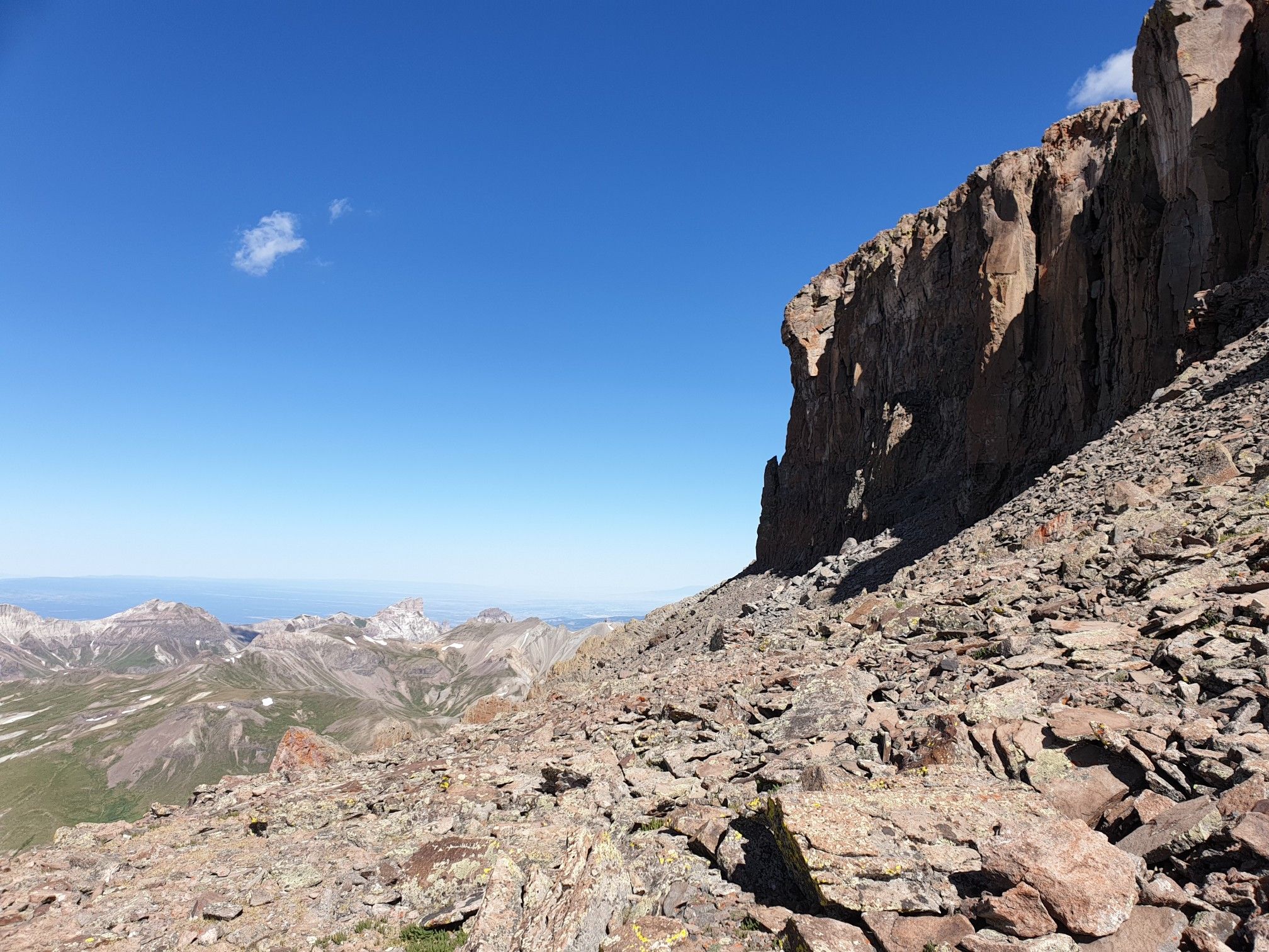 Sunny, rocky mountain slope with a steep cliff and distant peaks. - Wetterhorn Peak and Uncompahgre Peak
