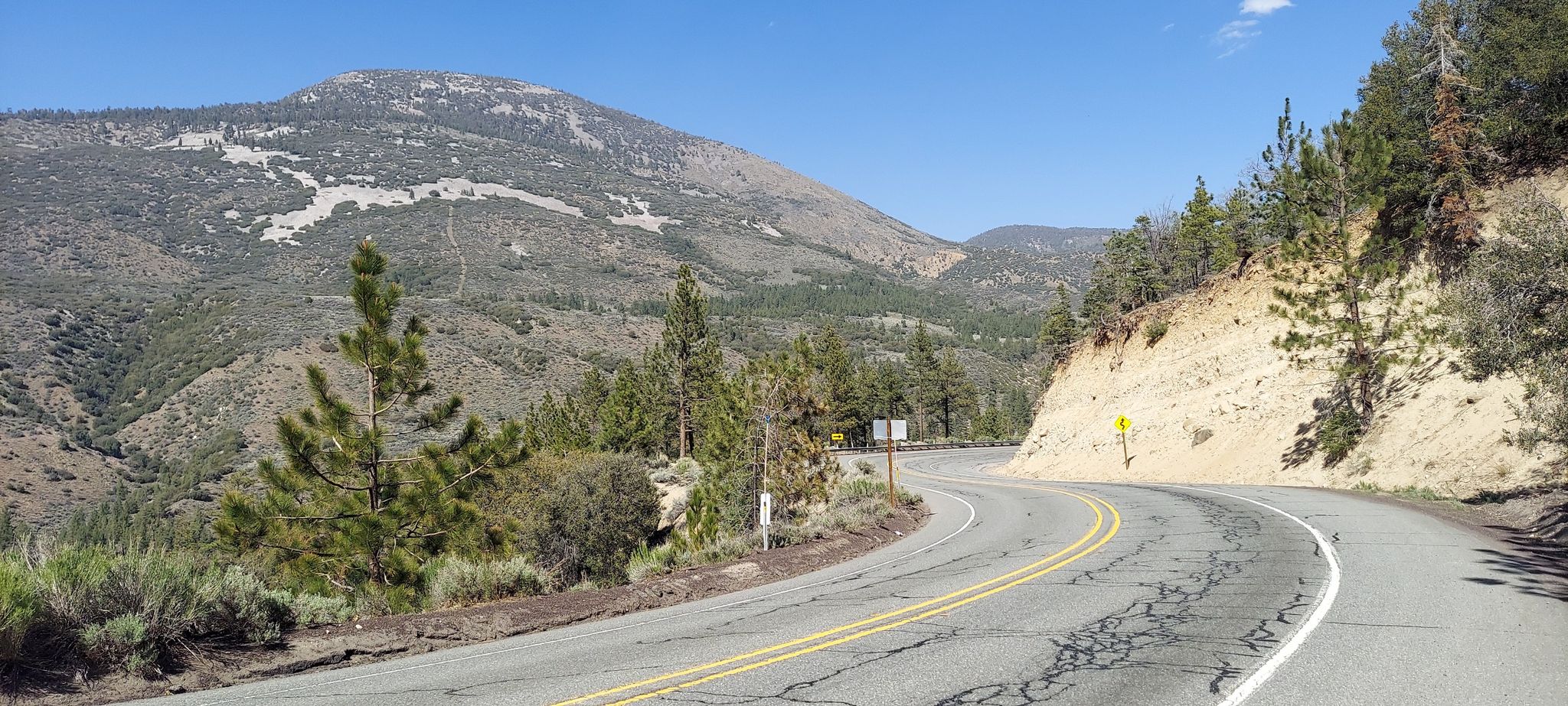 Winding mountain road with pine trees and a distant peak under clear skies. - Mill Creek Visitors Center to Onyx Summit