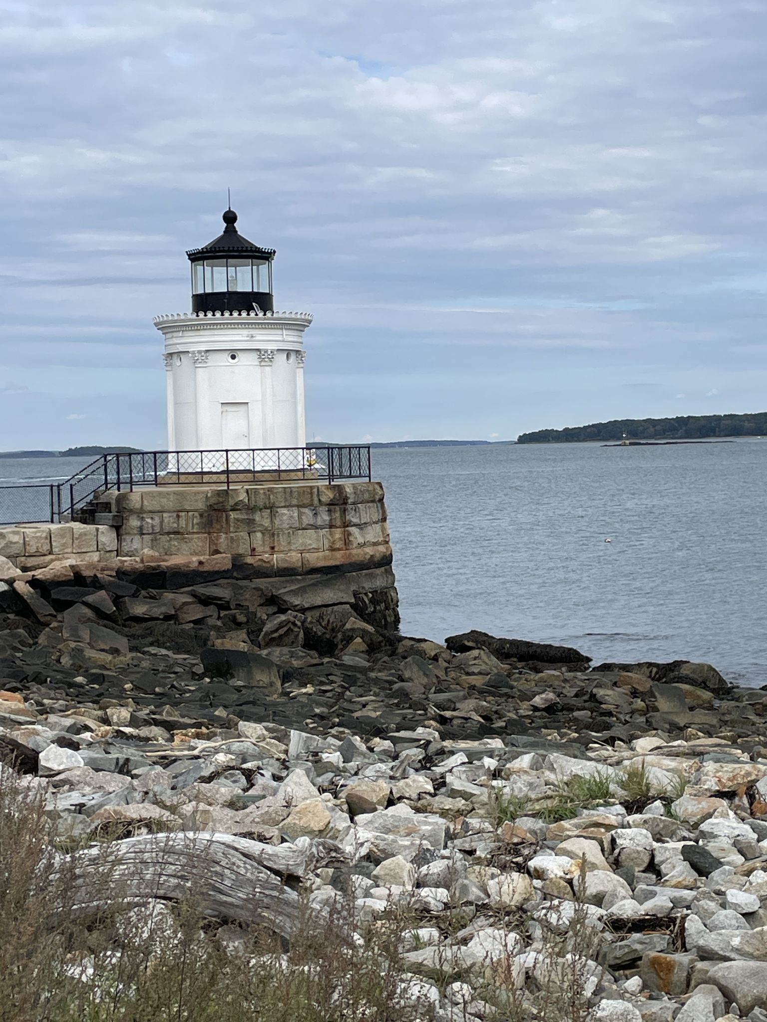White lighthouse on a rocky coastline under an overcast sky. - Bug Light Park – Spring Point Ledge Lighthouse loop from Southern Maine Community College